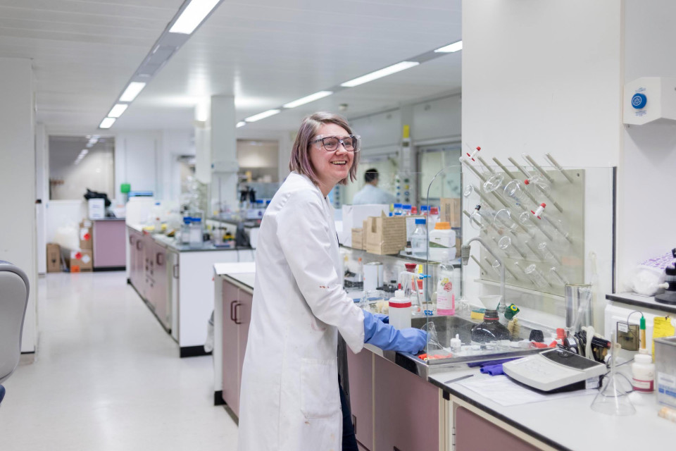 A woman smiling in a lab wearing protective glasses