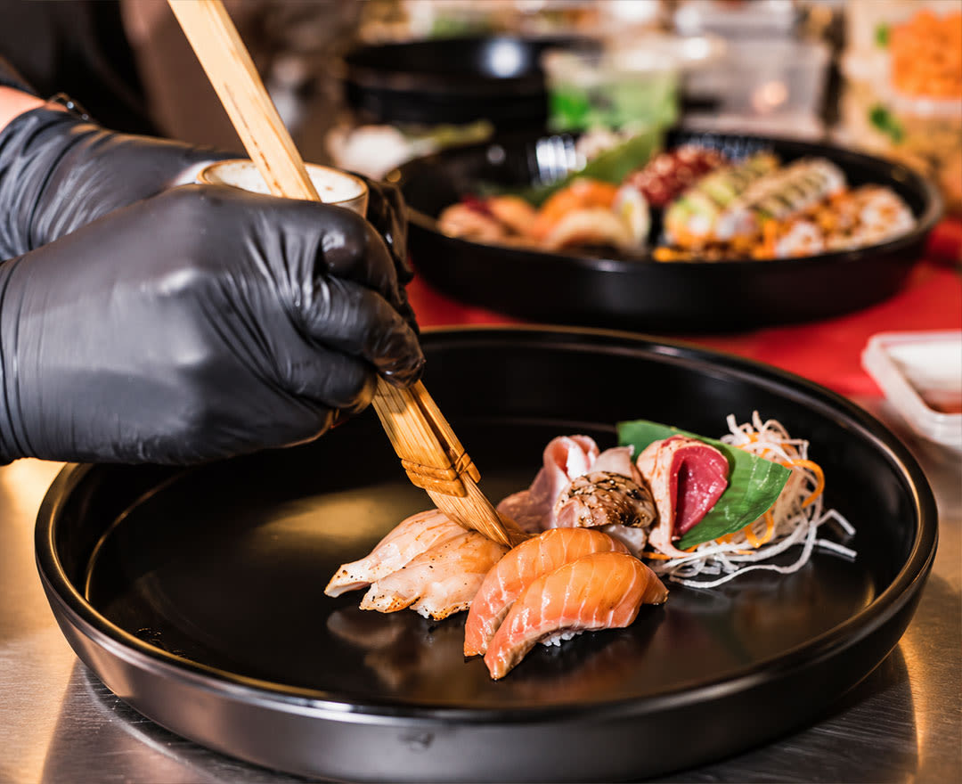 Un chef apporte la touche finale à des sushis garnis d’ingrédients colorés, servis avec une sauce crémeuse.