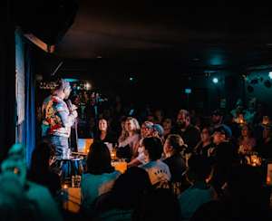 Une salle comble, des éclats de rire et un humoriste sur scène dans une ambiance chaleureuse et intimiste.