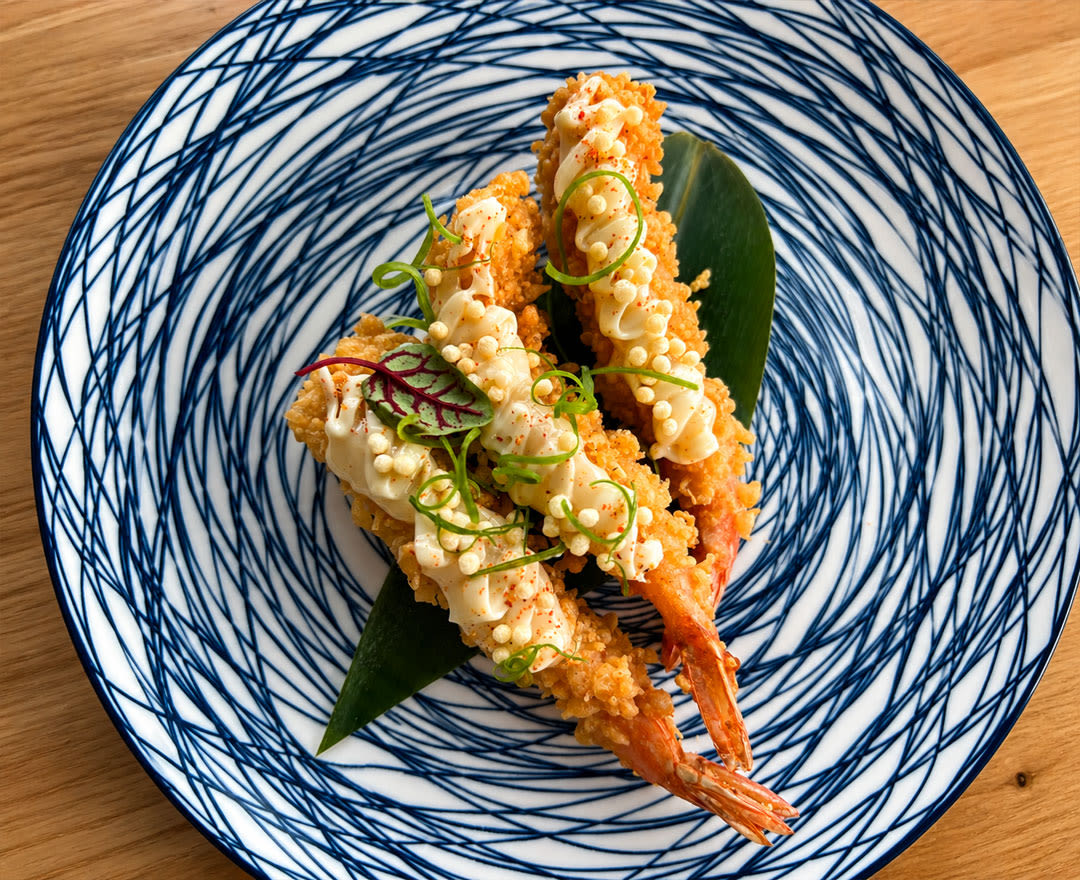 Crevettes tempura croustillantes, garnies de sauce crémeuse et de fines herbes, servies dans une assiette aux motifs bleus.
