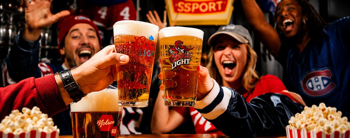 Des personnes souriantes trinquent avec des verres de bière Coors Light, entourées de popcorn, dans une ambiance festive.