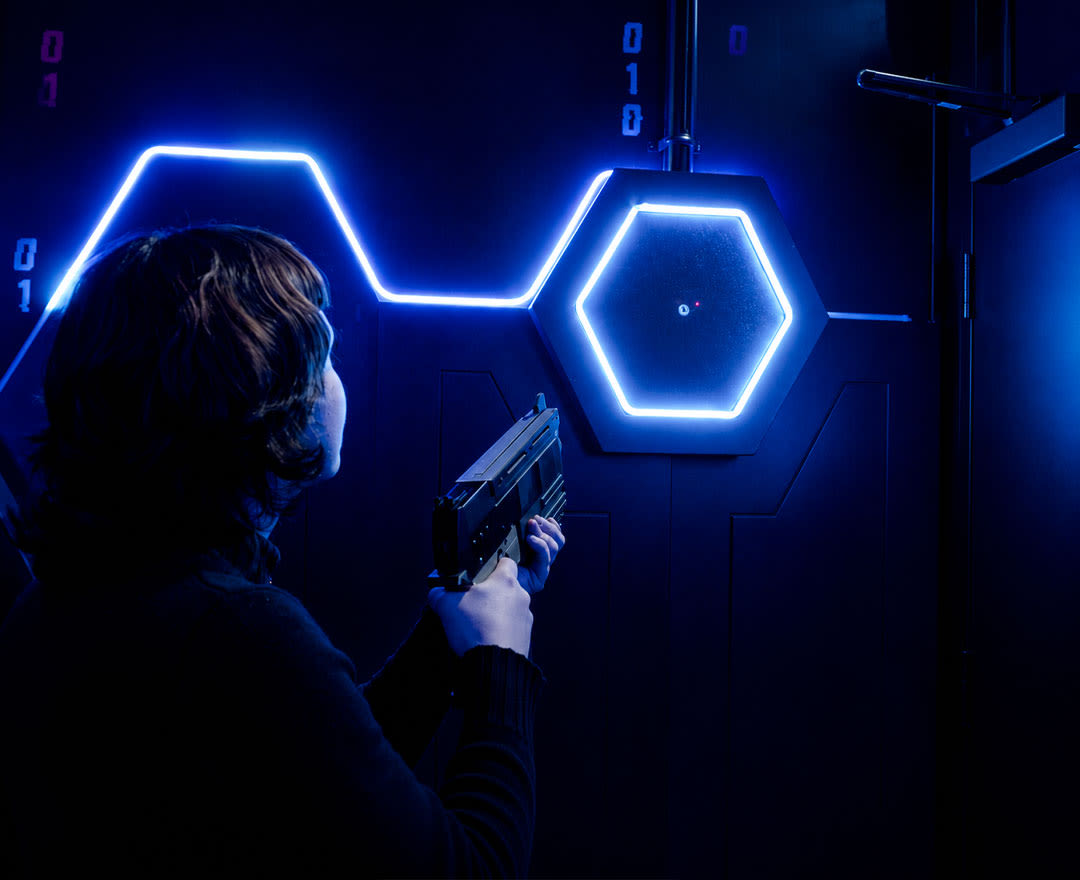 Deux personnes relèvent un défi interactif dans une salle immersive aux éclairages néon.