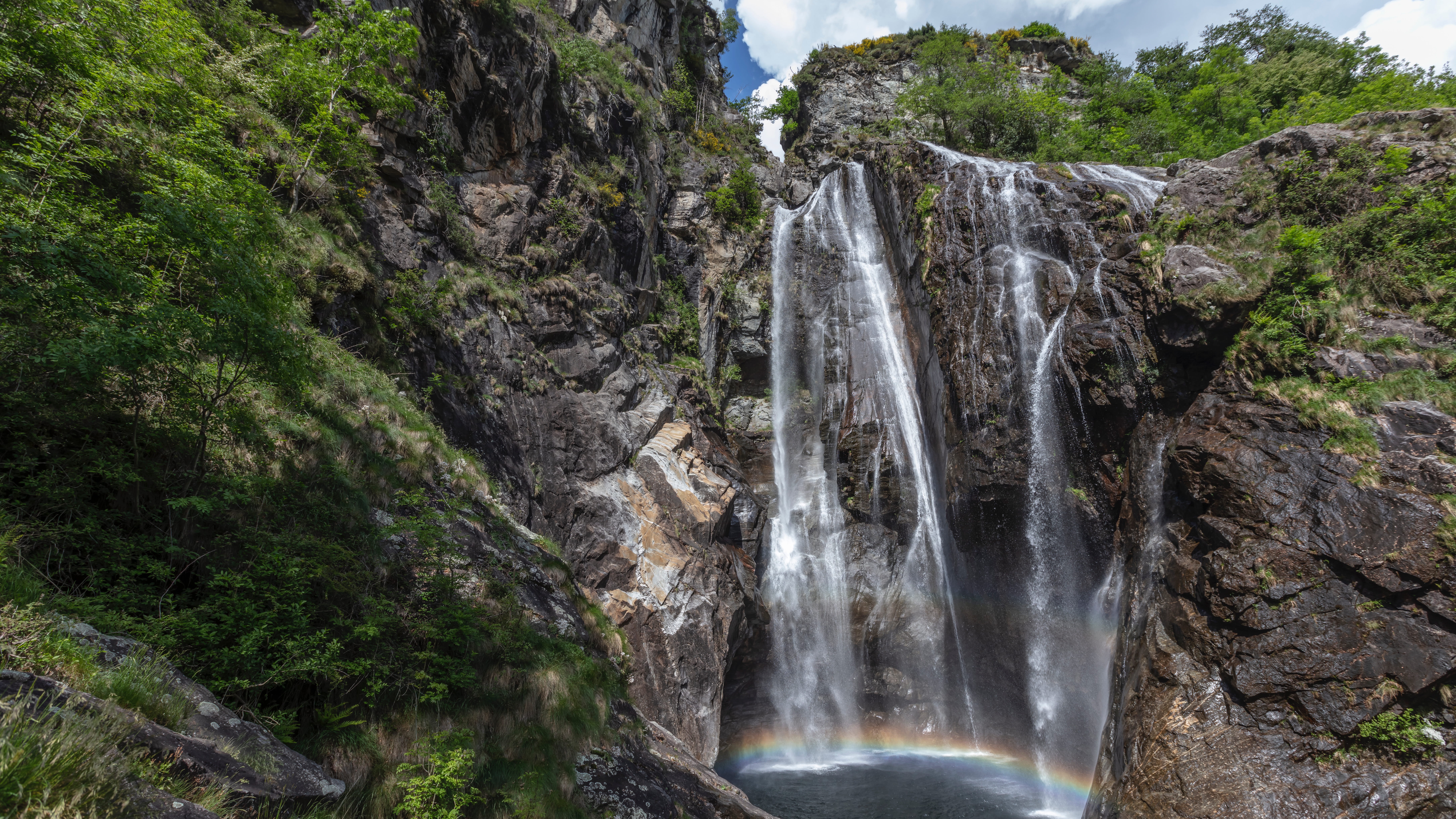 Wasserfall Cascata del Salto im Maggiatal, der über Felsen in ein natürliches Becken stürzt, mit einem kleinen Regenbogen im Sprühnebel.