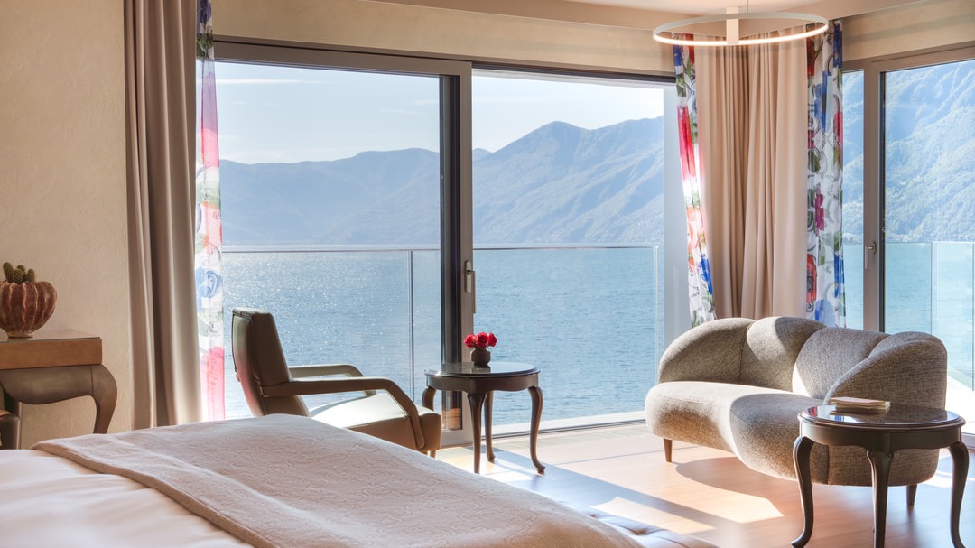 Exclusive suite featuring a cozy double bed, lounge chair, curved sofa, and floor-to-ceiling windows with direct views of the lake and mountains.