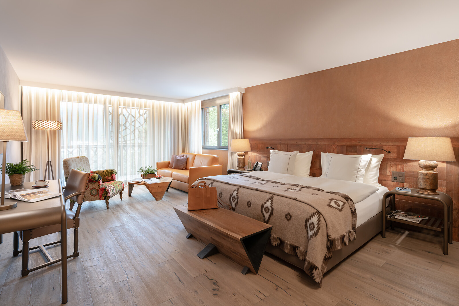 Großzügiges Junior Suite Zimmer mit kombiniertem Wohn- und Schlafbereich, Doppelbett, Sofa, Sitzecke und großen Fensterfronten mit viel Tageslicht.