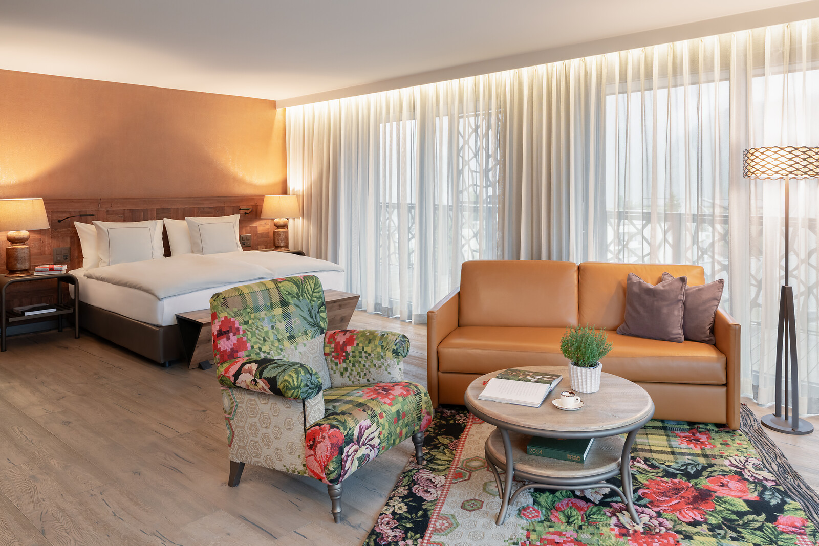 Modernes Hotelzimmer-Interieur mit weißem Bett, grün gemustertem Sessel und warmem Lichtdesign.