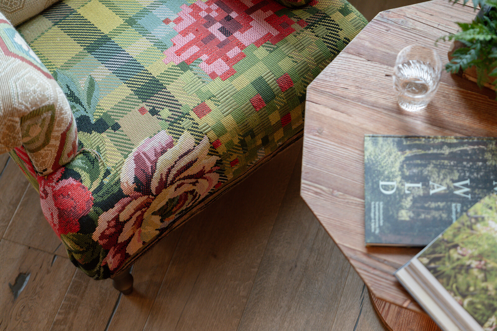 Close-up of a patterned armchair next to a wooden table with a book and glass as decorative interior accents.
