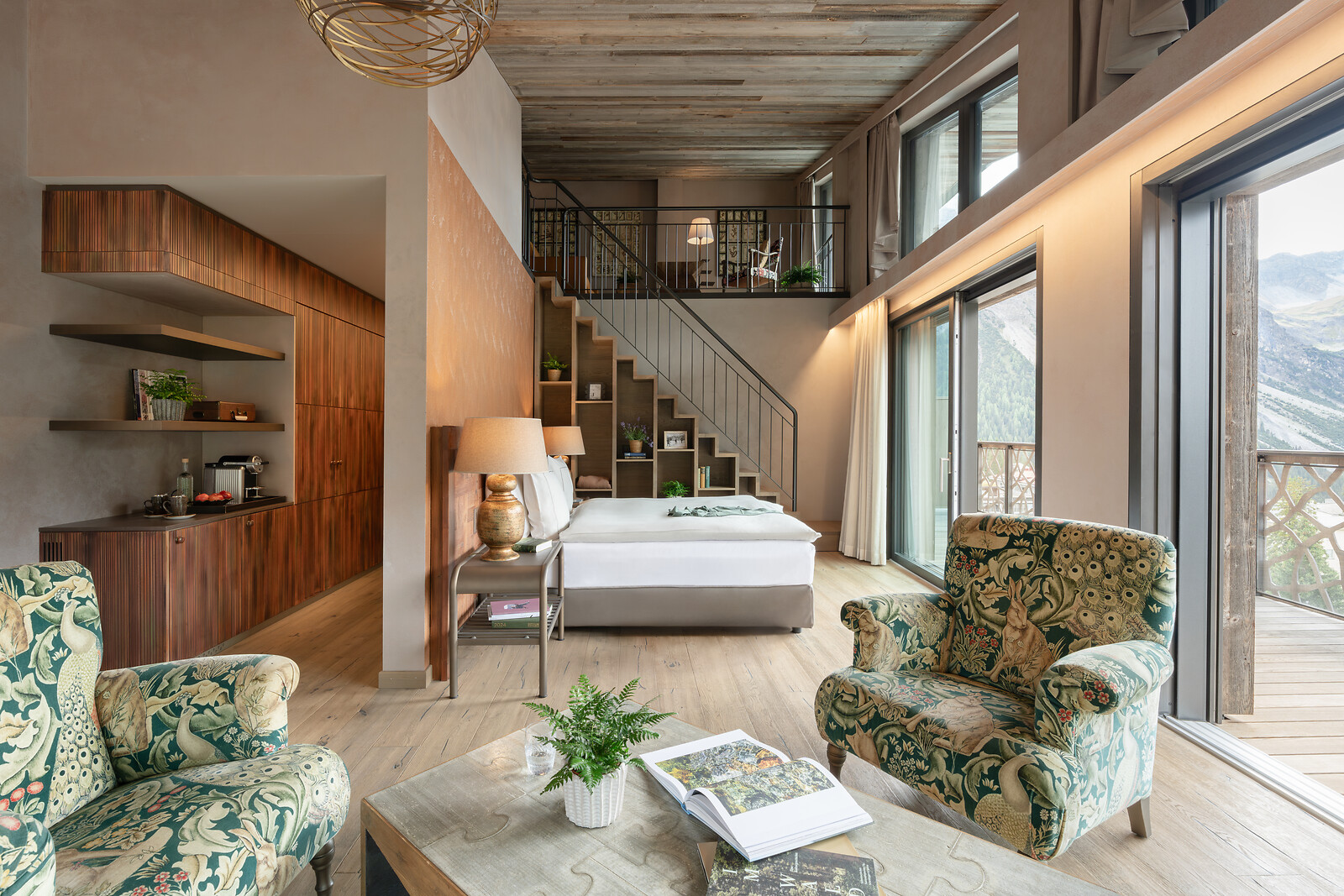 Großzügige Loft-Suite mit offenem Wohn- und Schlafbereich, Galerieebene, Treppe, stilvoller Sitzecke und großen Fensterfronten mit Bergblick.