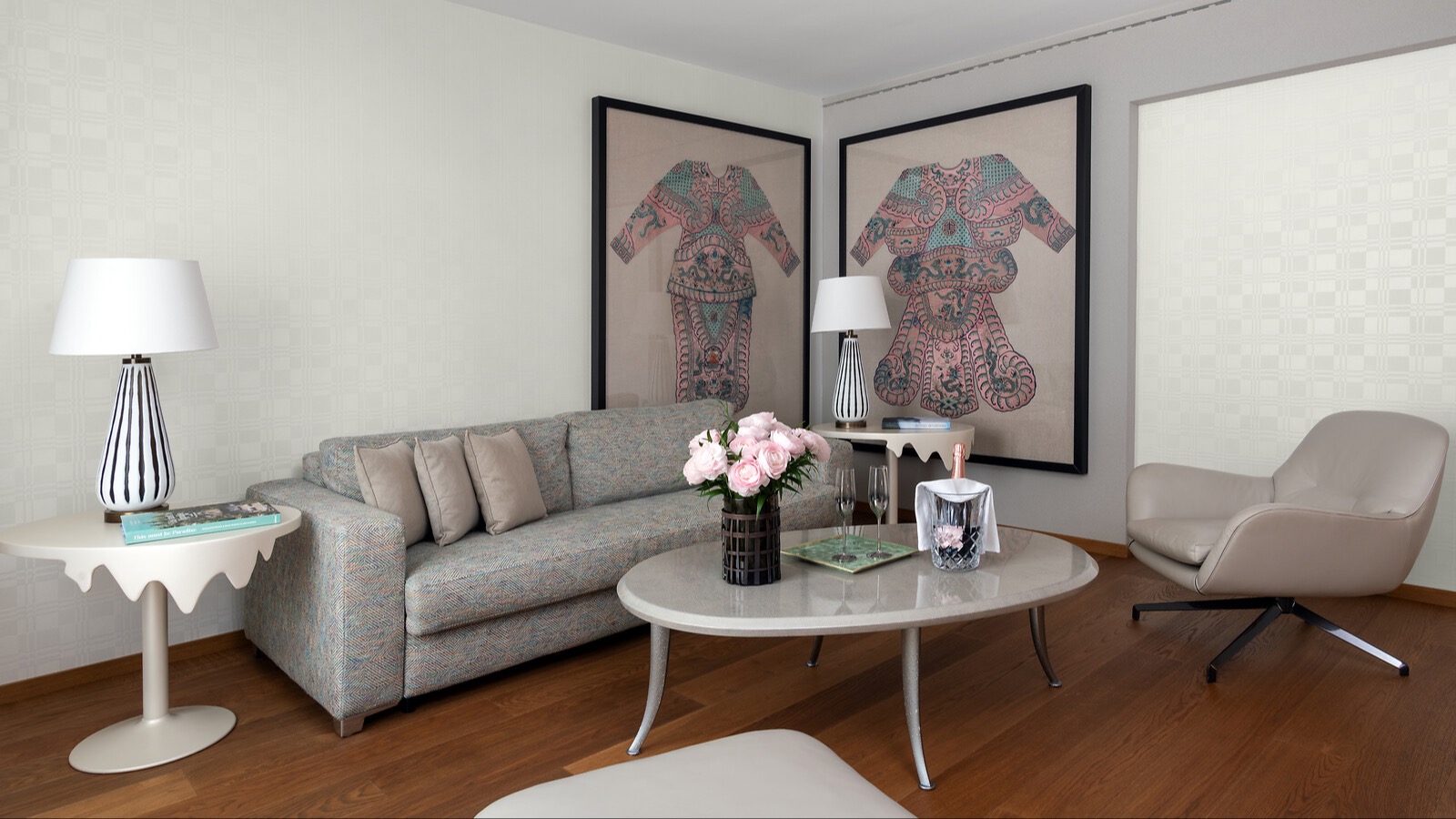 Stilvolles Wohnzimmer mit hellen Möbeln, moderner Couch, asiatisch inspirierten Kunstwerken, frischen Rosen und Champagner-Arrangement auf dem Couchtisch.