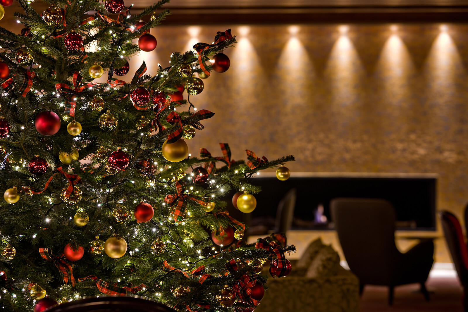 Prachtvoll dekorierter großer Weihnachtsbaum in einer eleganten Hotellobby, geschmückt mit roten Kugeln, roten Schleifen und transparenten Glaskugeln.