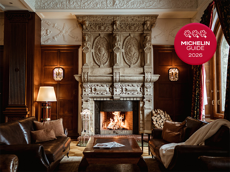 Elegant room with ornate stone fireplace, burning fire, leather furniture, and Michelin 2026 three-star badge in corner.