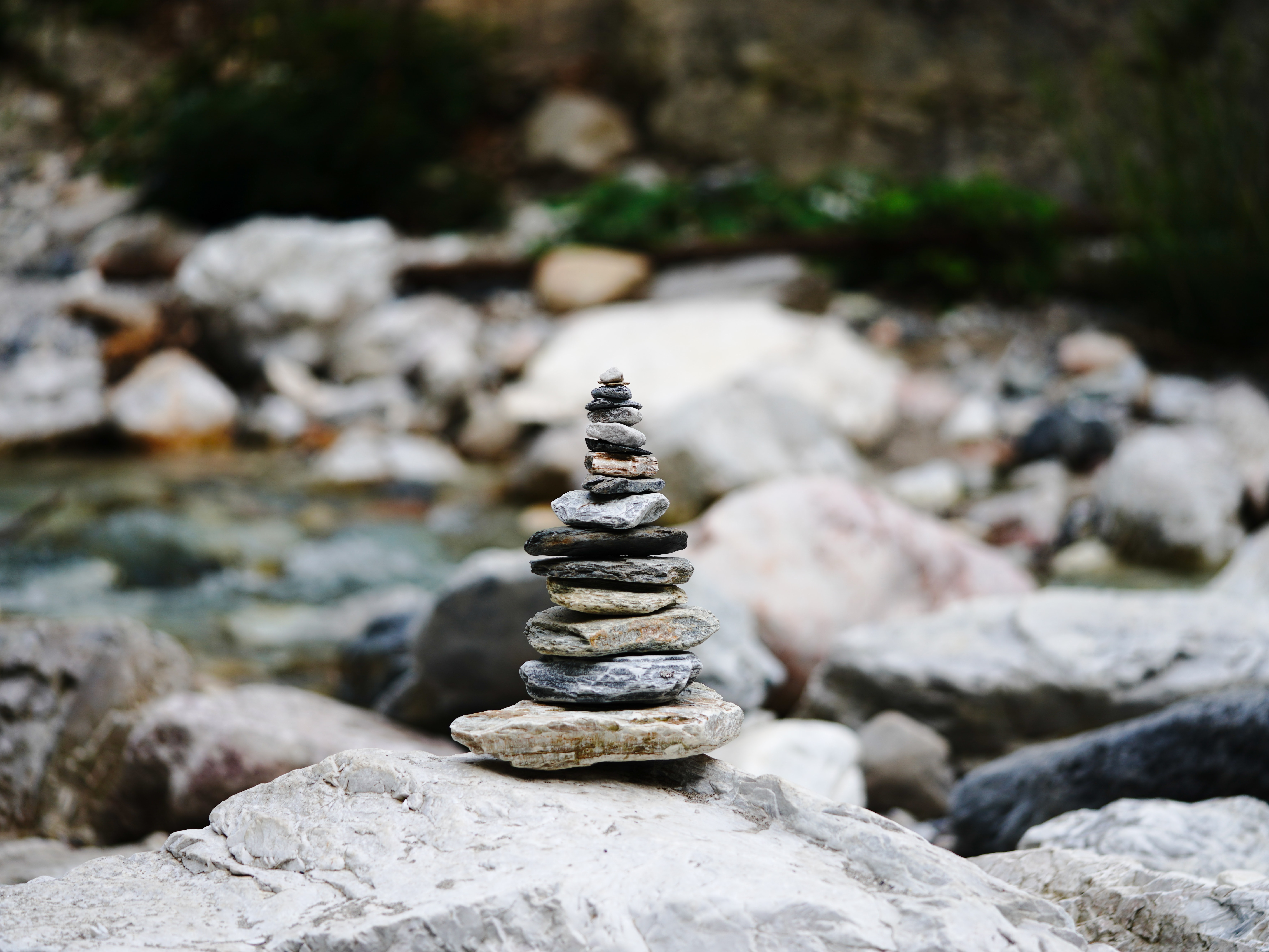 Stacked stones balanced in a tower formation on a rocky riverbed with blurred water and boulders in the background.