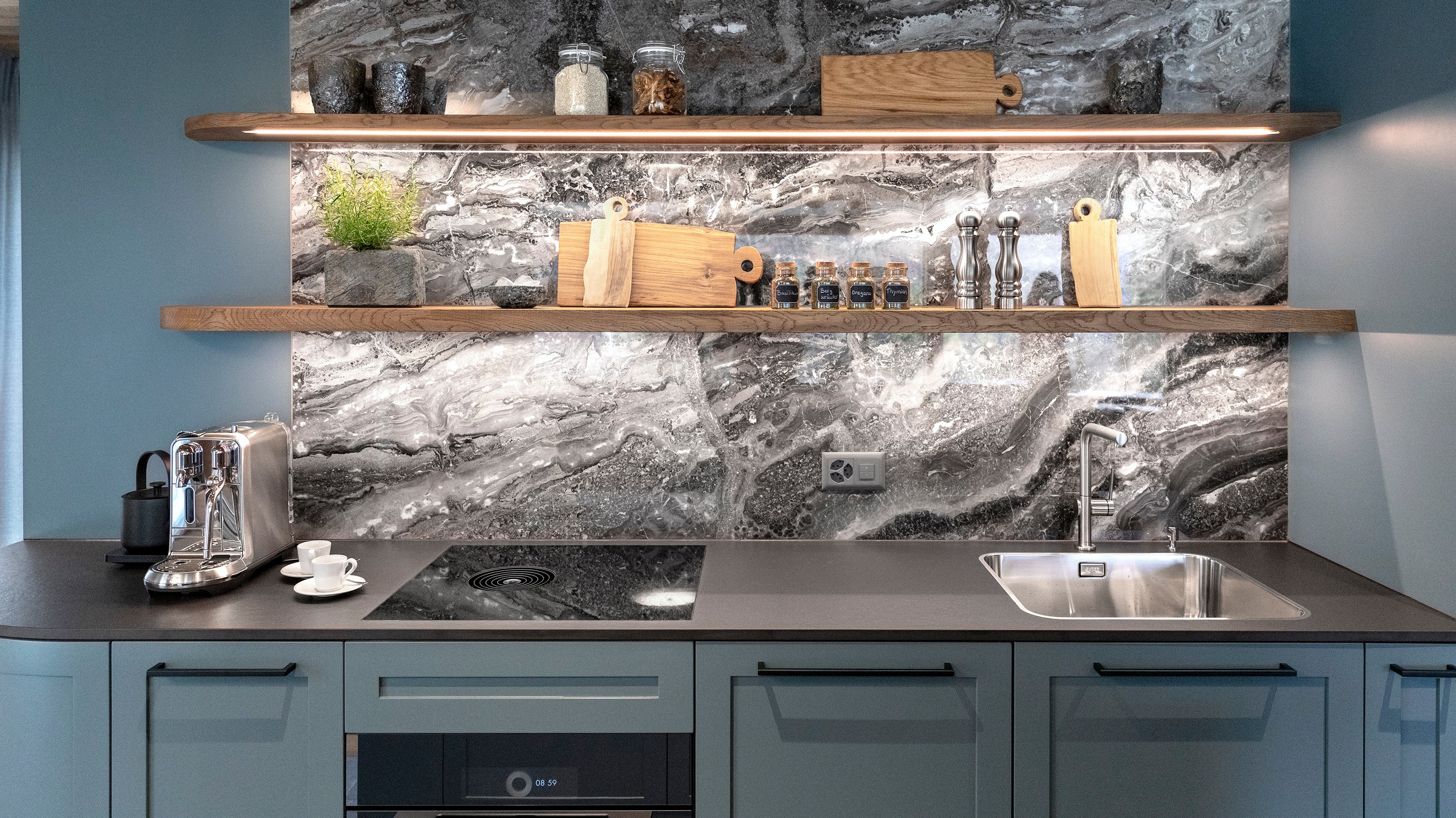 Modern kitchen with gray marble backsplash, wooden floating shelves, blue cabinets, and stainless steel sink and appliances.