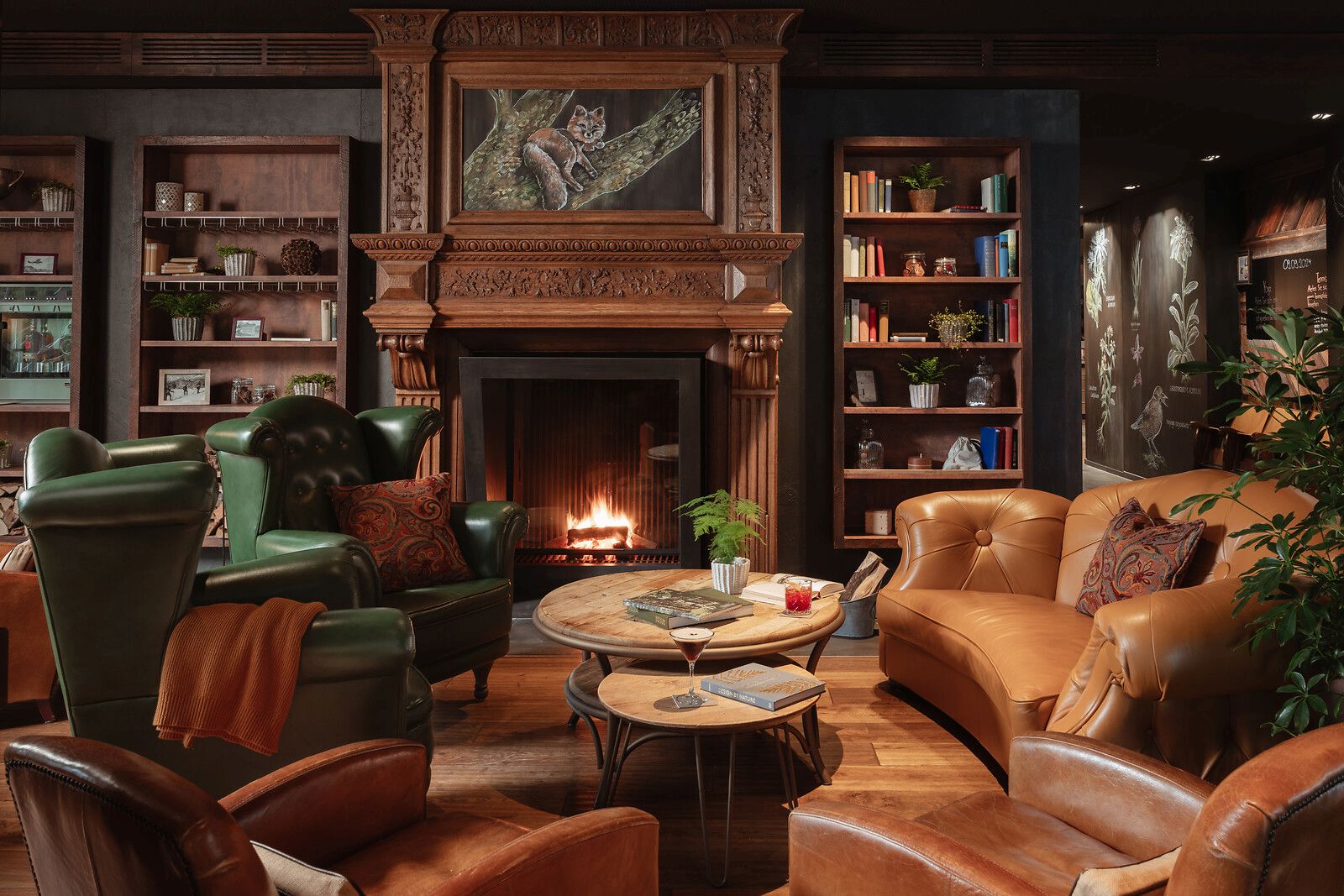 Elegante Bibliotheks-Lounge mit einem kunstvoll verzierten Holzkamin, ledernen Sesseln in Grün und Hellbraun, Einbauregalen und warmer Beleuchtung.