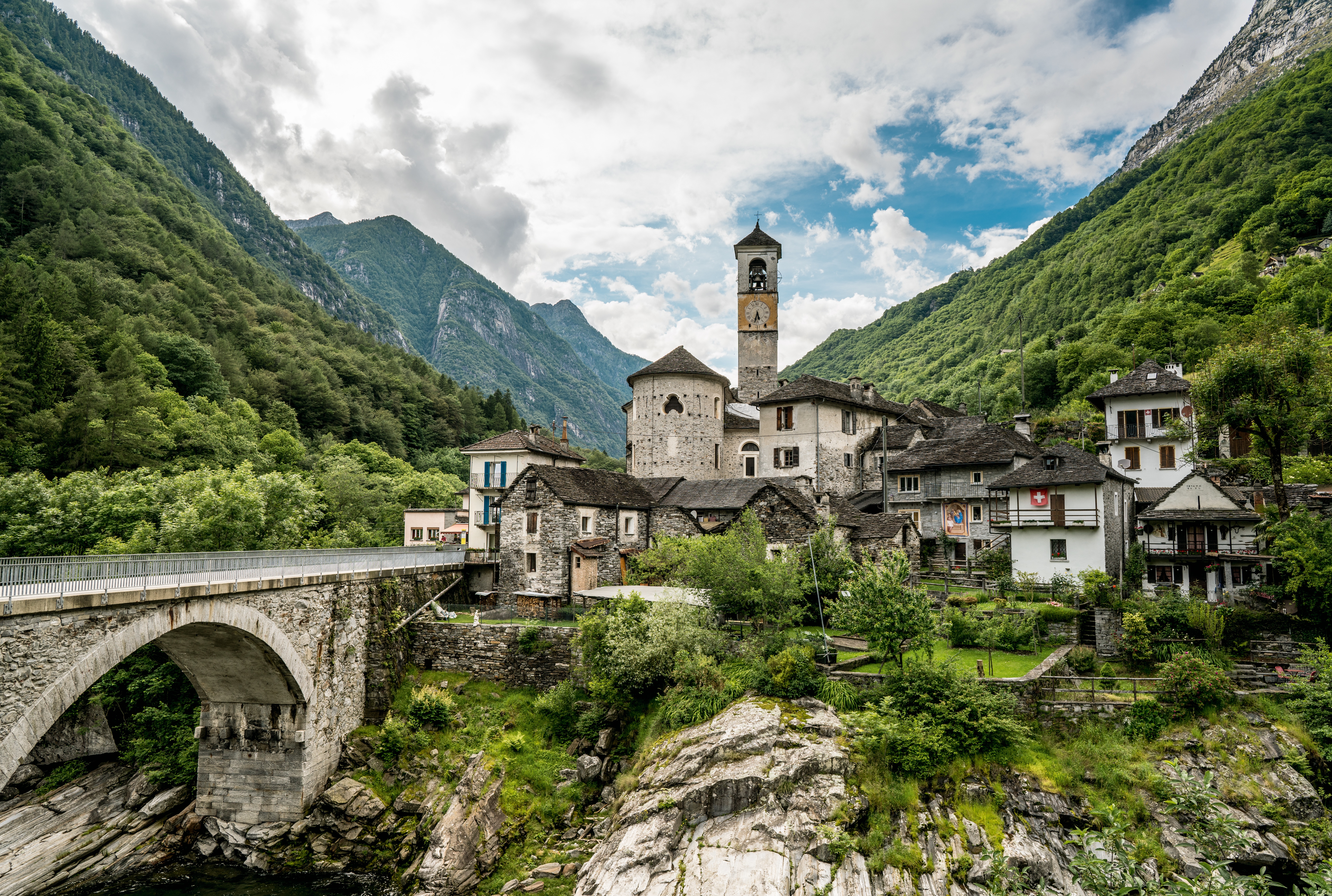 Historisches Dorf Lavertezzo im Valle Verzasca mit Steinbrücke, Kirchturm und traditionellen Häusern, umgeben von dicht bewaldeten Bergen.