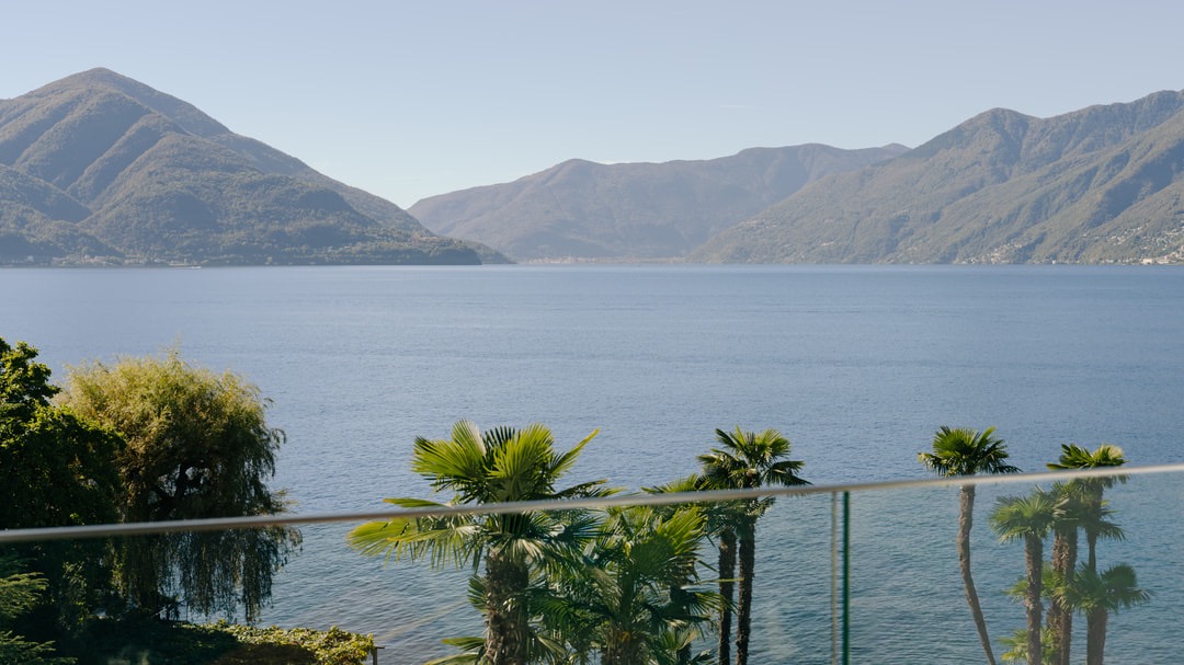 Atemberaubender Ausblick vom Hotelbalkon auf tiefblauen See, umliegende Berge und tropische Palmen im Vordergrund unter klarem Himmel.