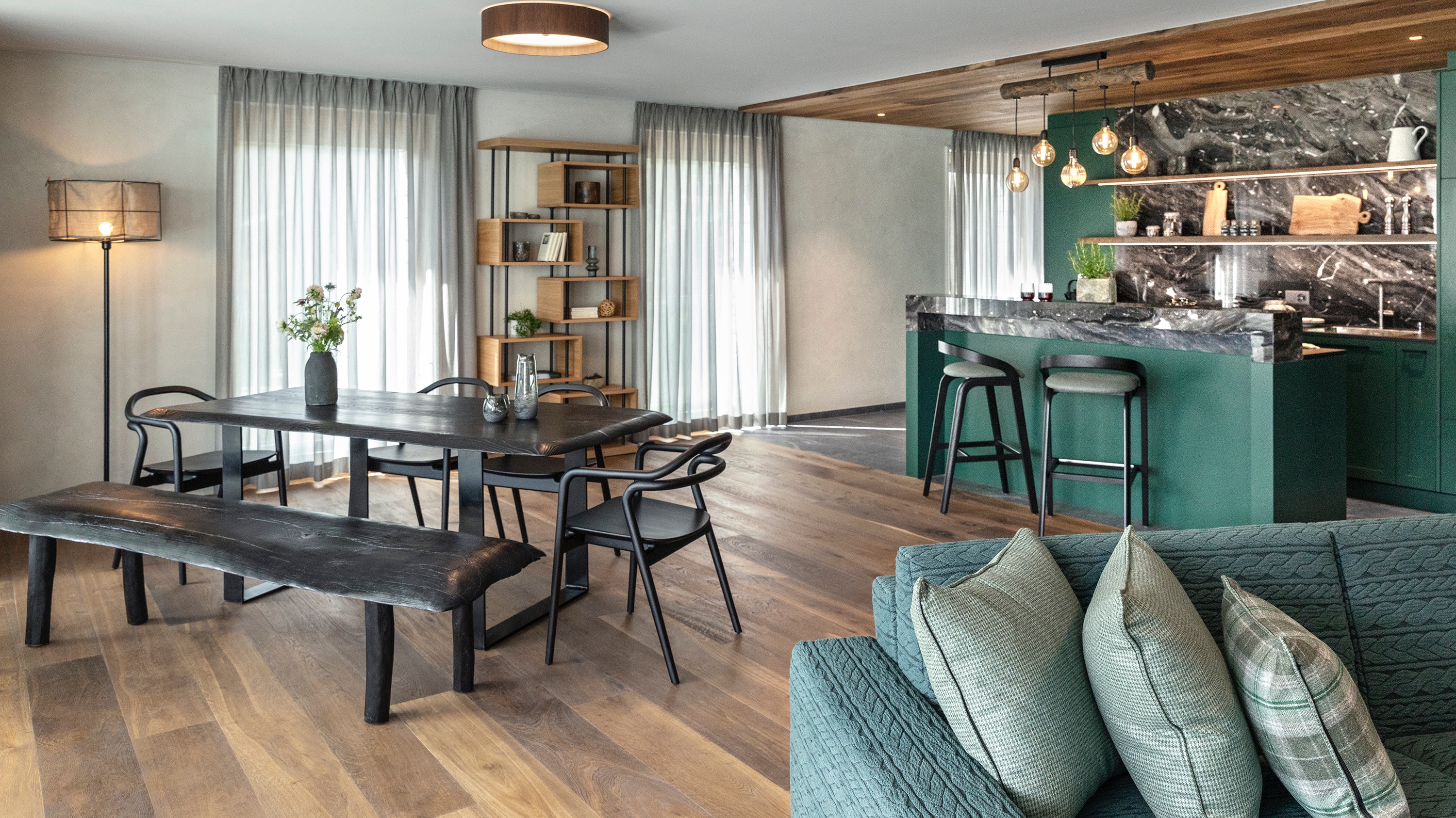 Moderner, offener Wohnbereich mit einem dunklen Esstisch, einer grünen Kücheninsel mit Marmor-Arbeitsplatte und einem blaugrünen Sofa.