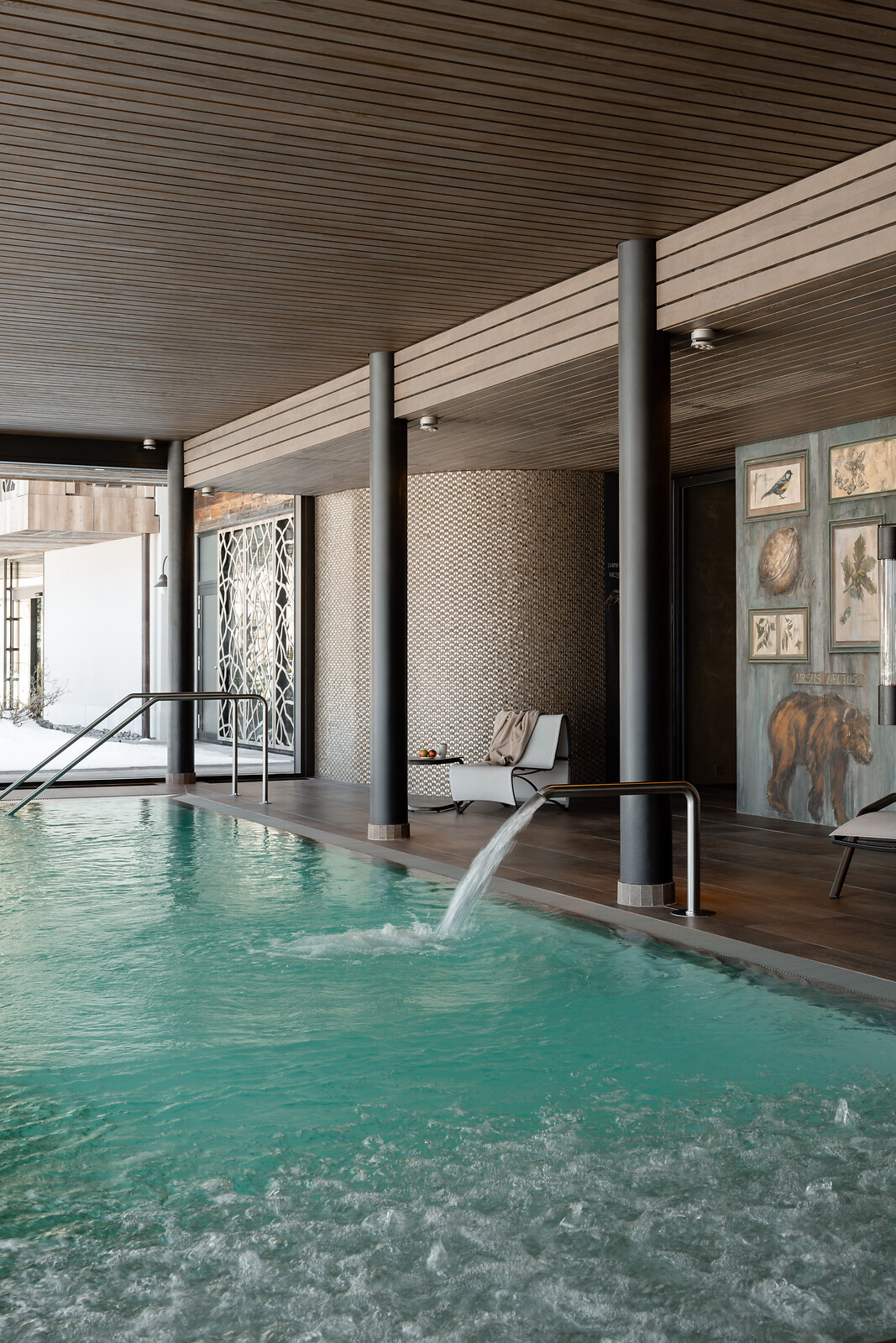 Indoor pool area with white lounge chairs, botanical wall art on weathered wood panels, and turquoise water in foreground.