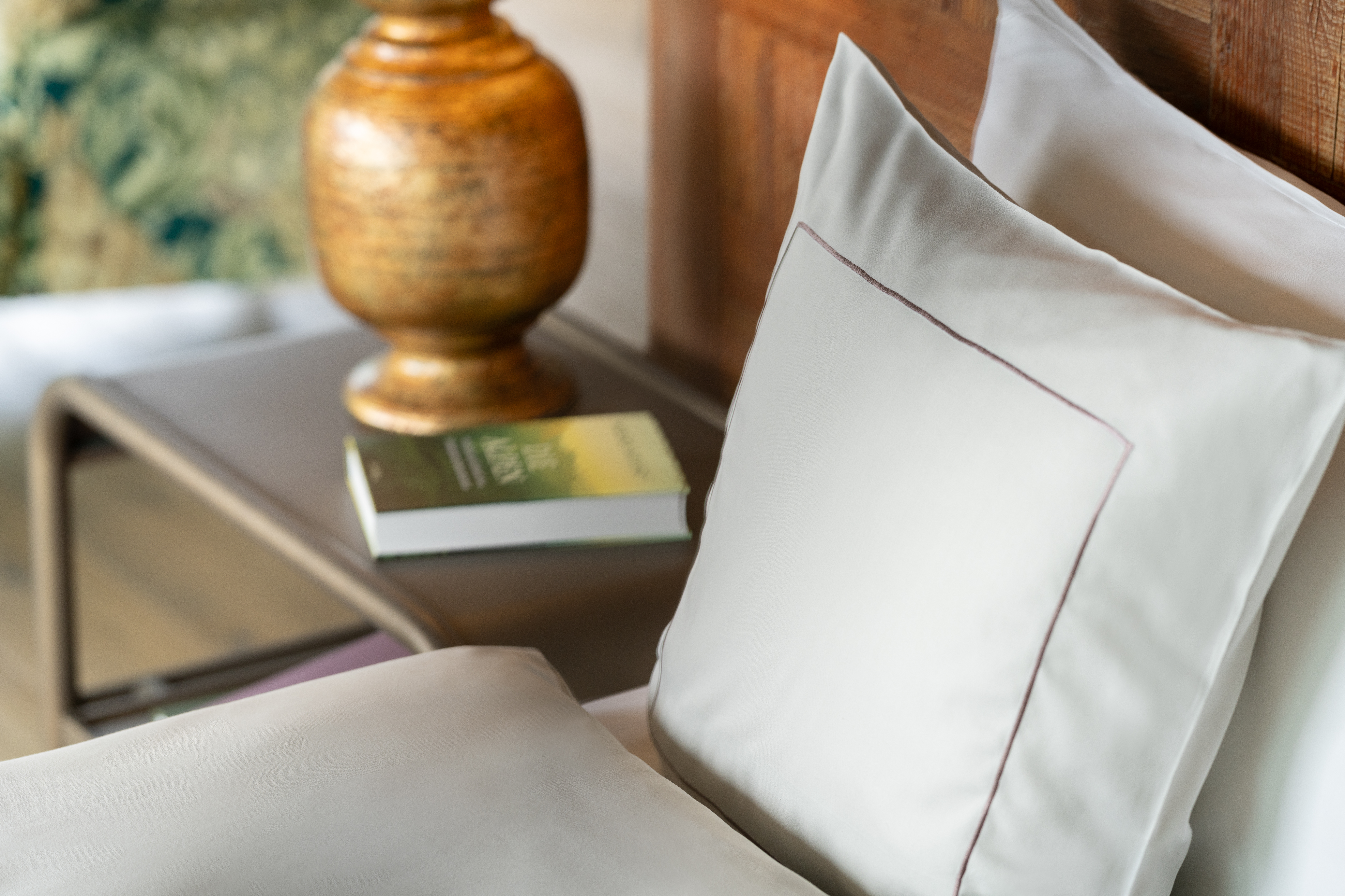 Close-up of a bed with large white pillows, a book on the nightstand, and warm shimmering light.