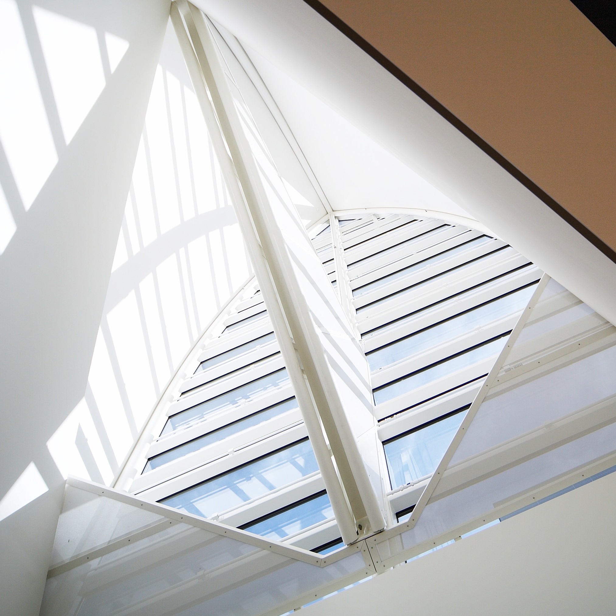 Blick von unten auf eine weisse Wendeltreppe mit Geländer und Sonnenlicht durch ein Dachfenster.