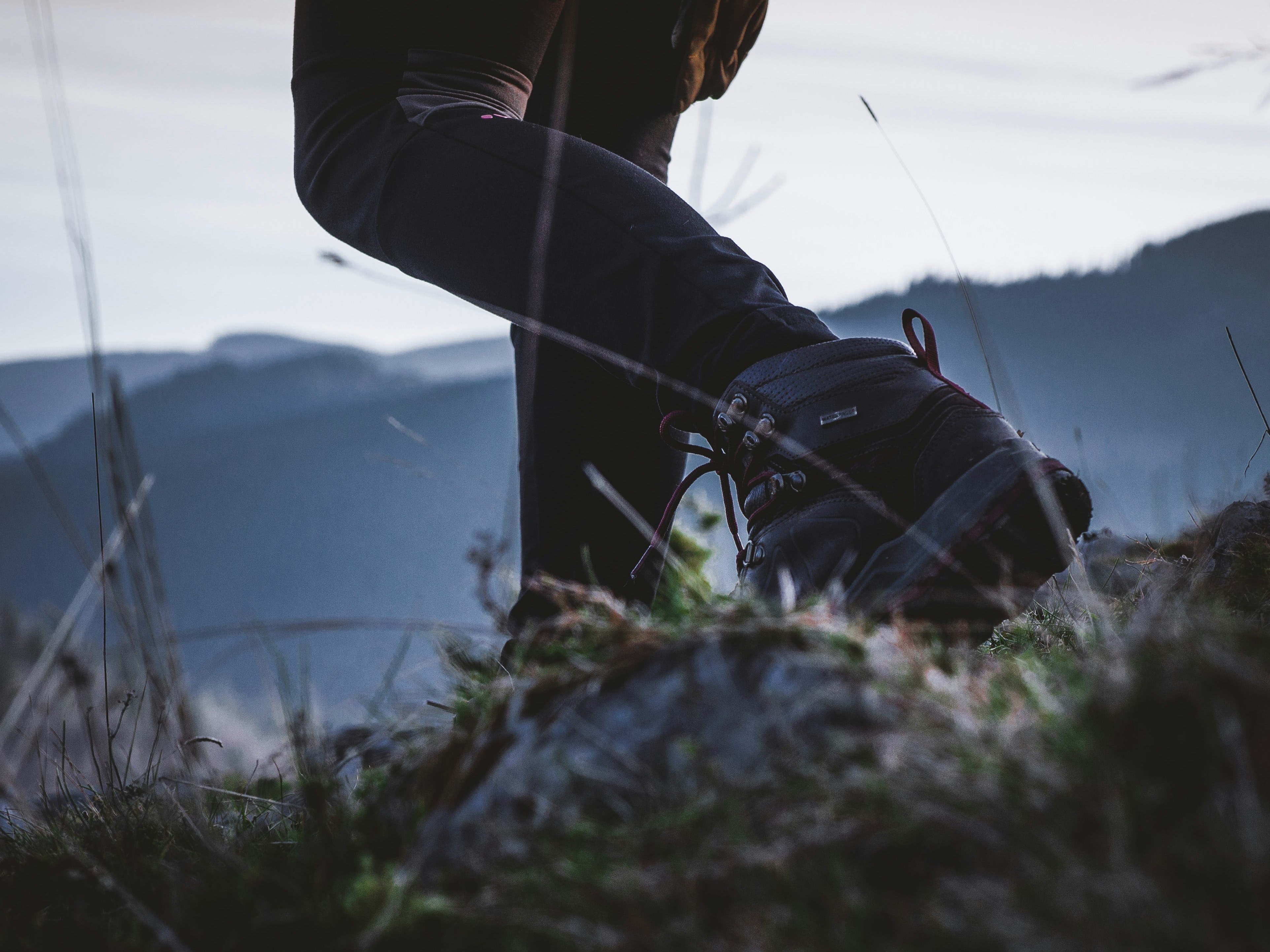 Close-up of a hiker's black boot stepping on rocky terrain with mountains in the background.