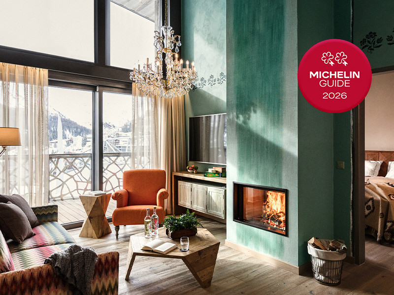 Luxury hotel suite with crystal chandelier, turquoise fireplace, orange armchair, mountain views, and Michelin 2026 badge.