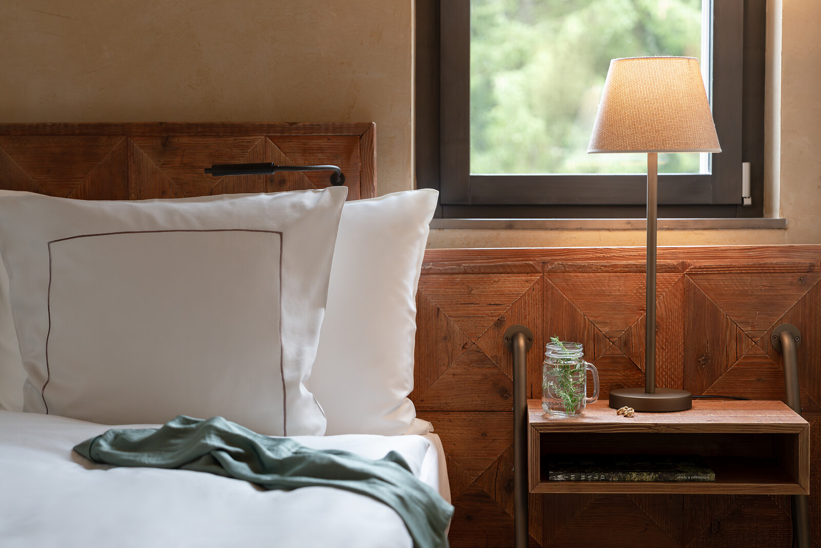 Cosy hotel room at Valsana Hotel Arosa with a white bed, wooden details, bedside lamp and views of the greenery outside.
