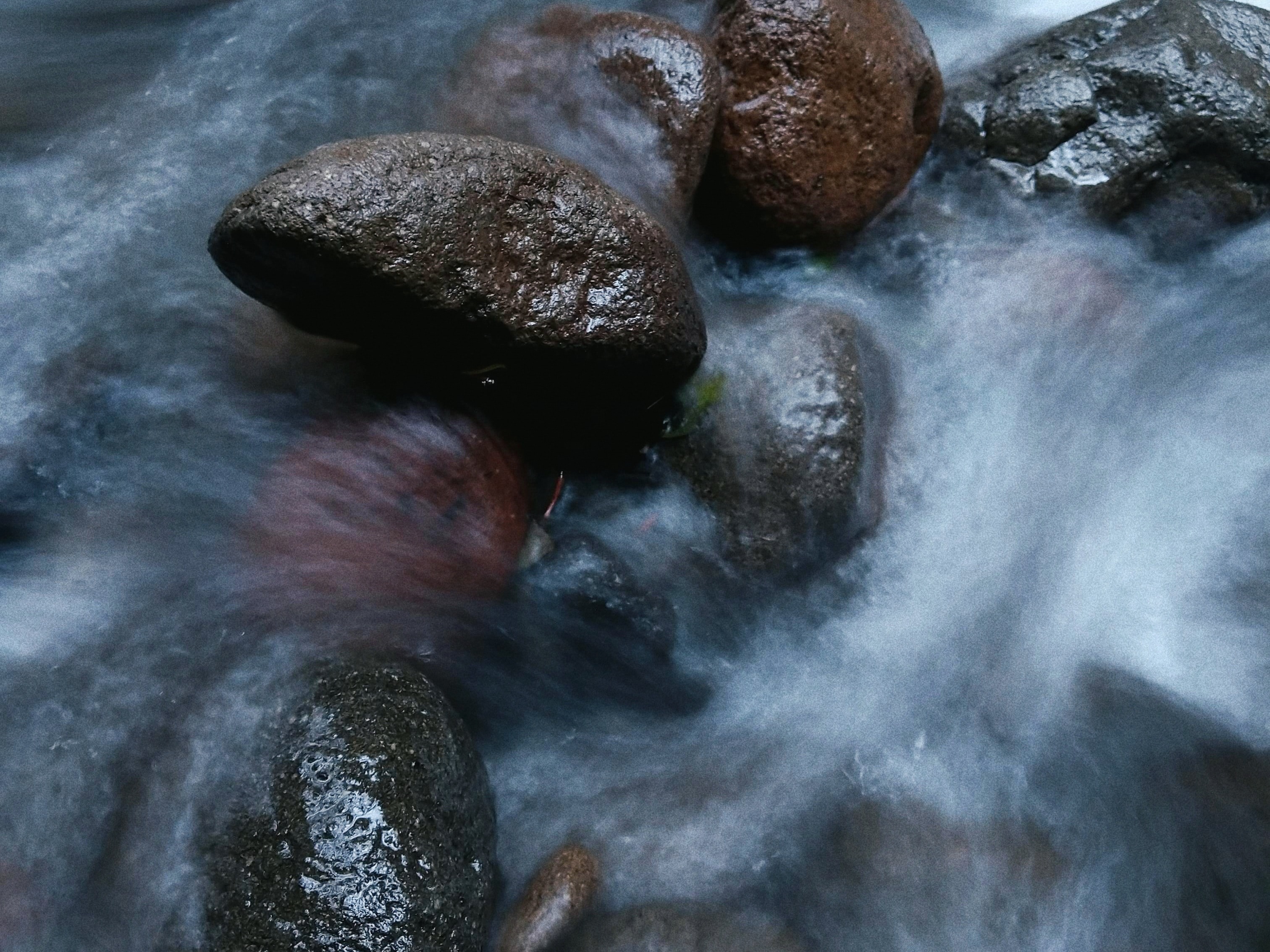 Smooth brown and gray rocks in flowing stream water.