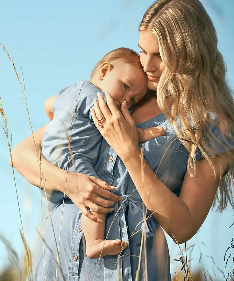 Woman holding baby close against a daytime sky.