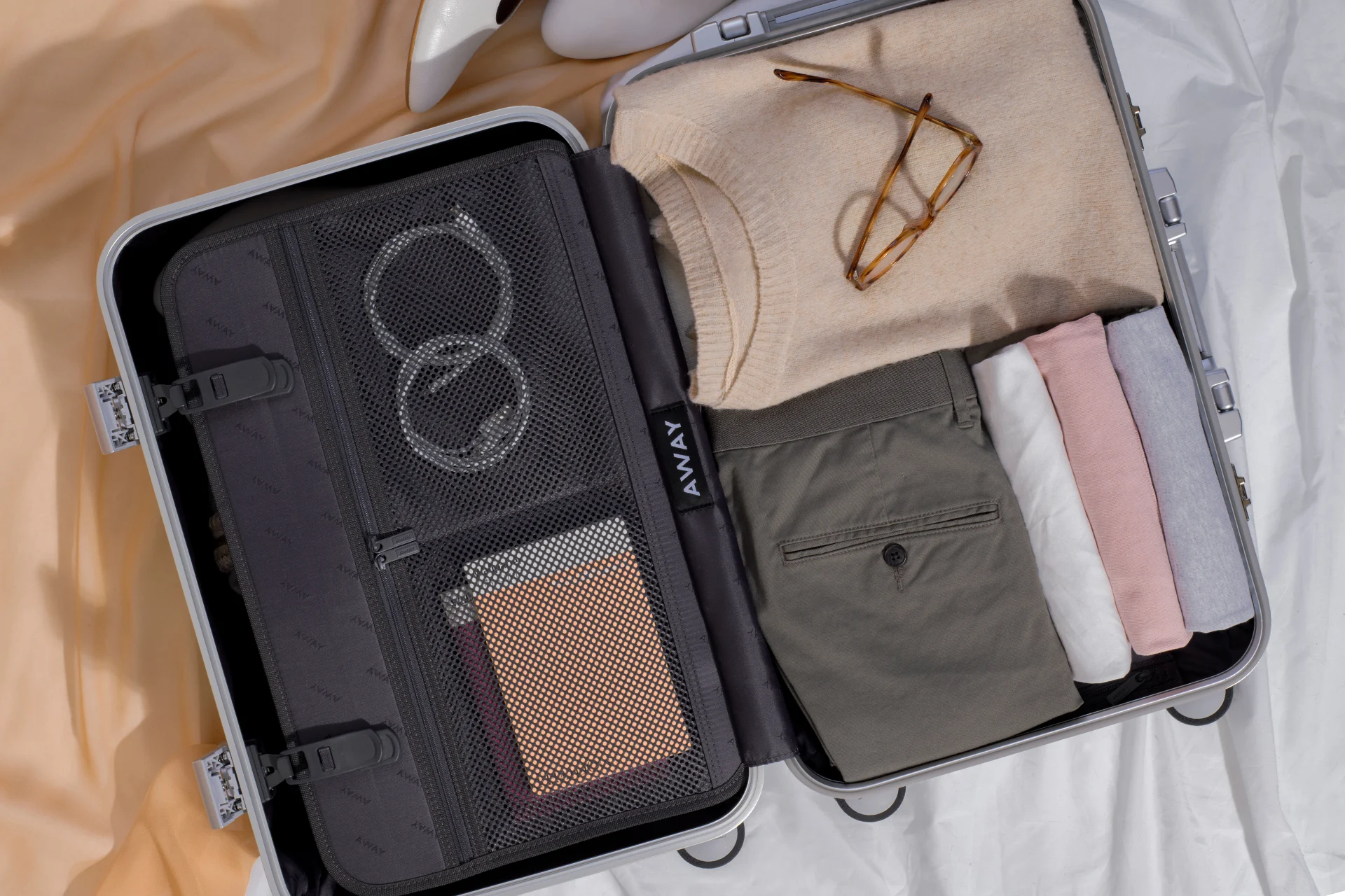 An Aluminum suitcase opened to reveal a clip in mesh pocketed panel folded clothes on the right side.
