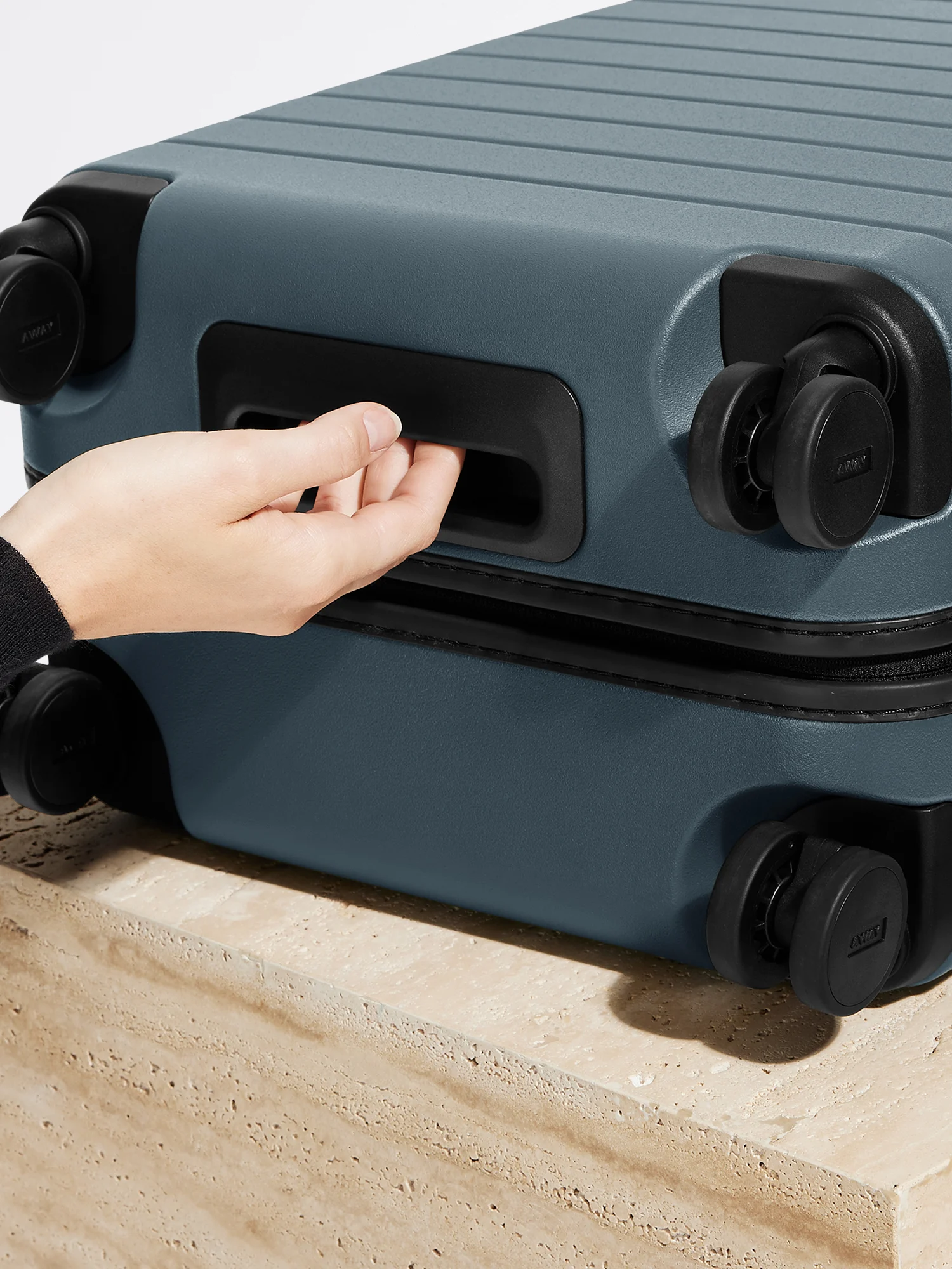 Person grabbing the underside handle of an Away suitcase for easy lifting