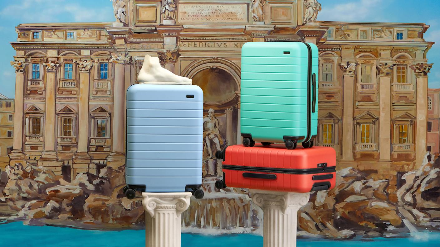 Three Away suitcases in red, light blue and sea green on two columns with The Trevi Fountain in the background.