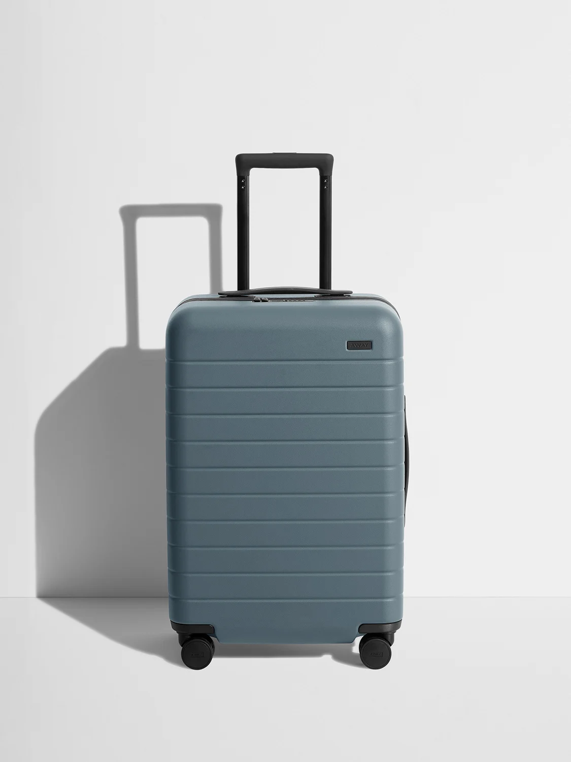  A Coast blue Away Bigger Carry-On suitcase with wheels on a white surface.