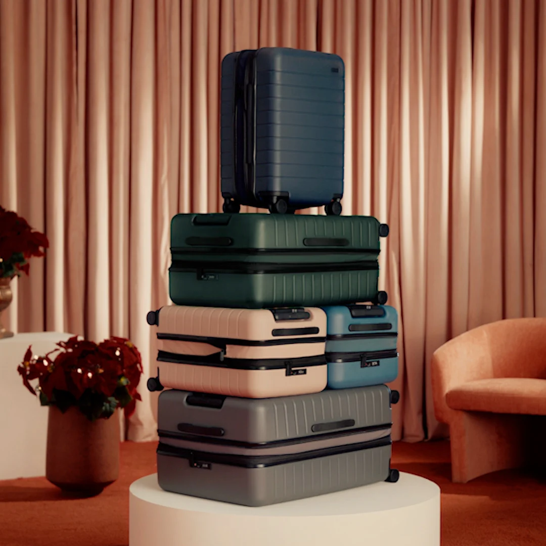 Away Flex suitcases piled on a white plinth