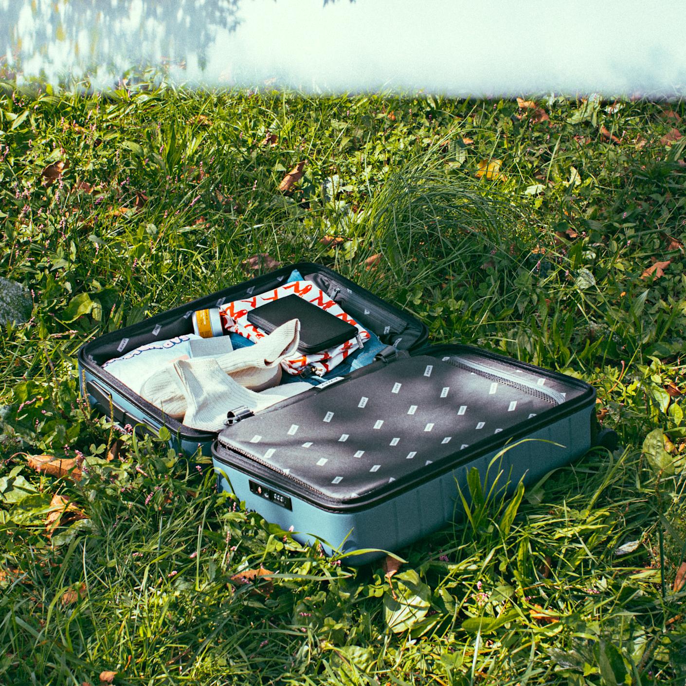 An open blue carry-on suitcase open in the middle of a grassy ground packed with internal compression showing.