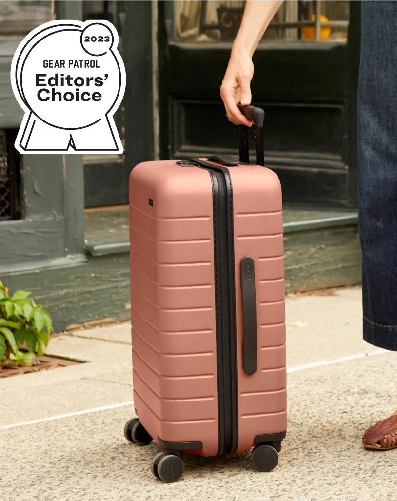 Someone picking up the Away best-selling Bigger Carry-On in Clay Pink