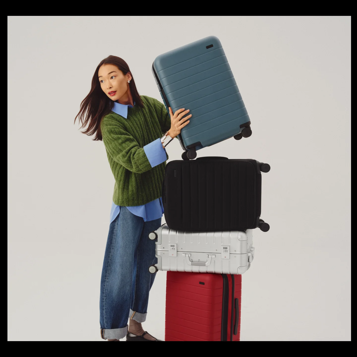 Person holding an Away Bigger Carry-On suitcase next to a stack of other Away carry-on luggage