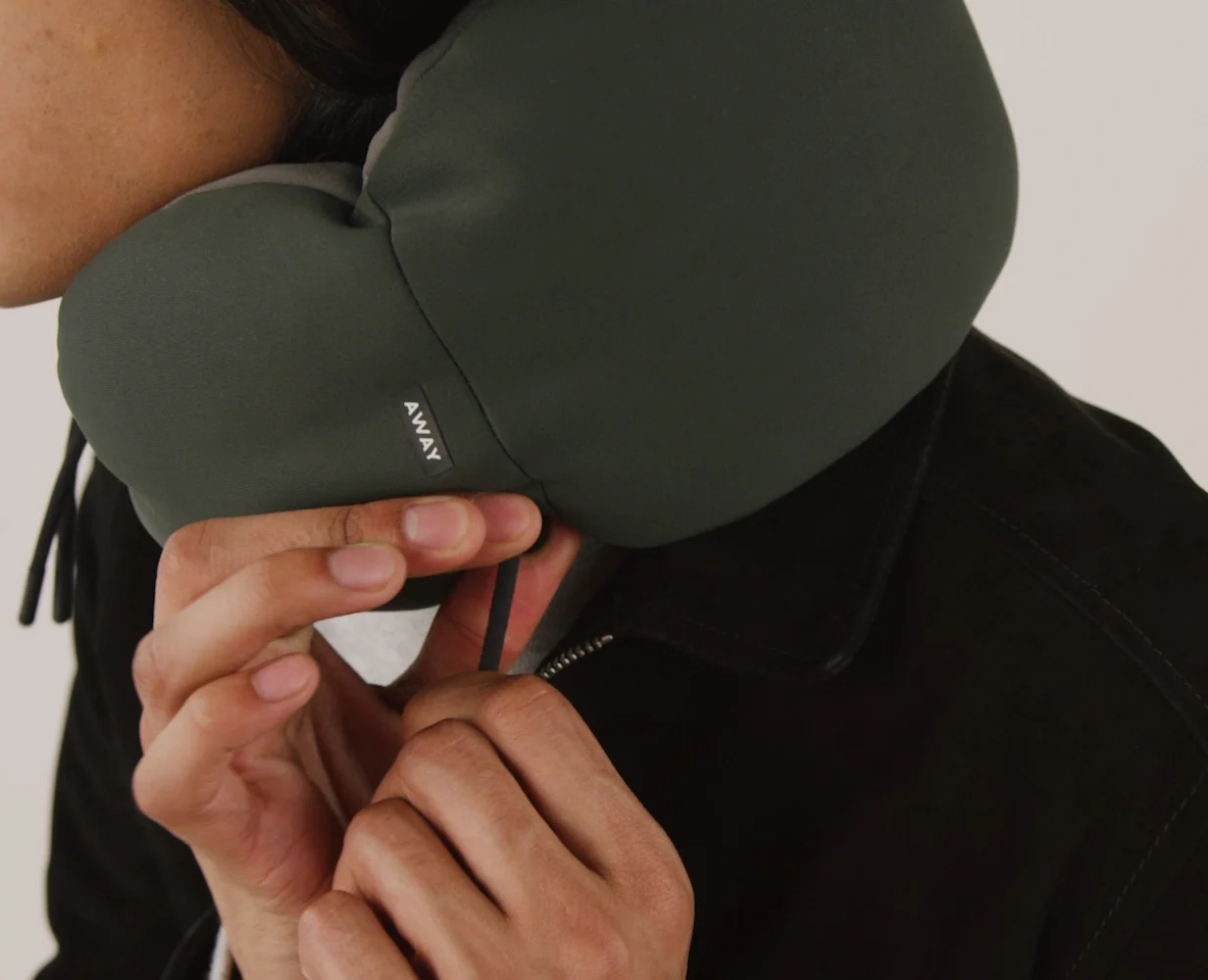 A person adjusting their Away travel neck pillow in green for comfort.