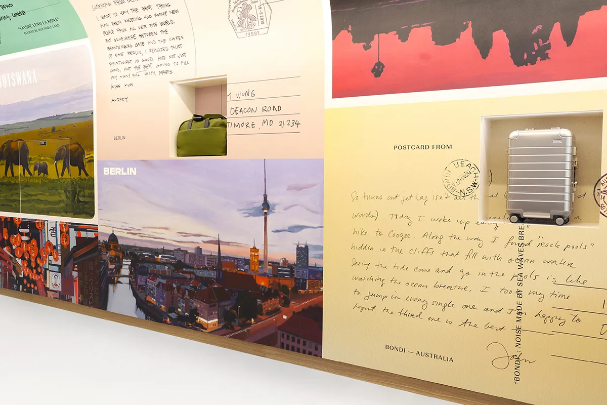 A mural of postcards displayed on a wall with luggage displayed within it.