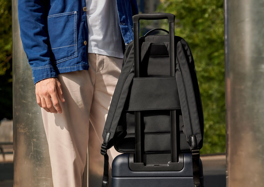 The Backpack in black sitting on top of navy suitcase secured by a sleeve that attaches the Backpack to the suitcase handle.