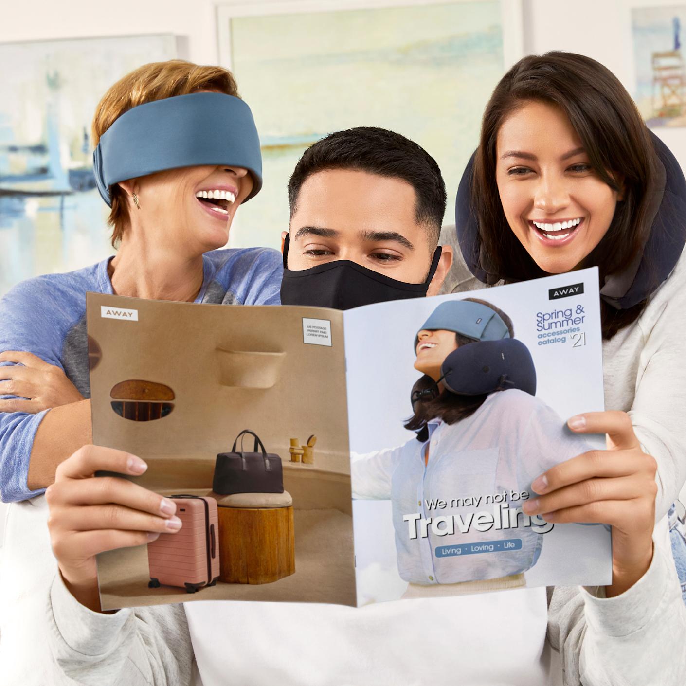 People looking through the Away catalogue on travel packing accessories wearing a sleep mask, reusable cloth face mask and neck pillow.