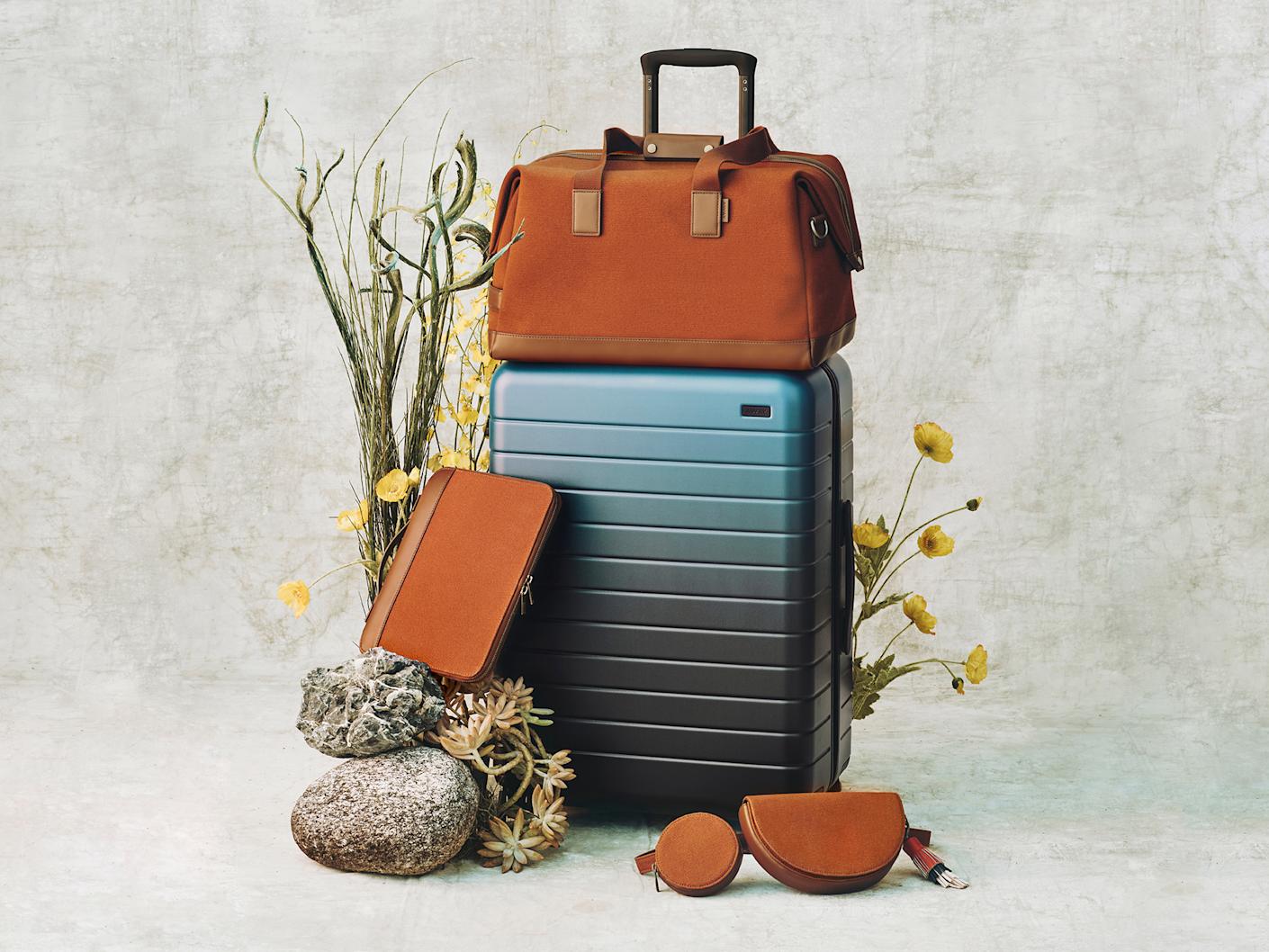 Luggage displayed with a cabin suitcase in metallic blue, a brown duffle bag, tablet case and sling bag.