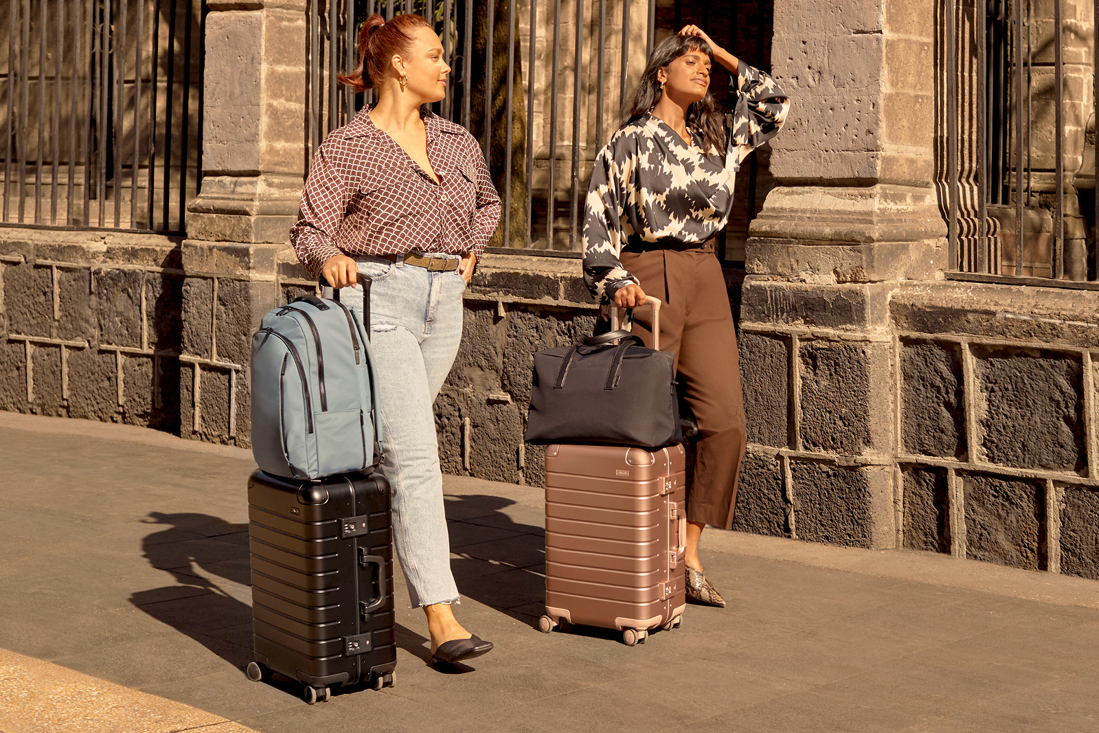 Two women strolling down a street with their travel bags, a backpack and duffle bag paired with aluminum carry-on suitcases.