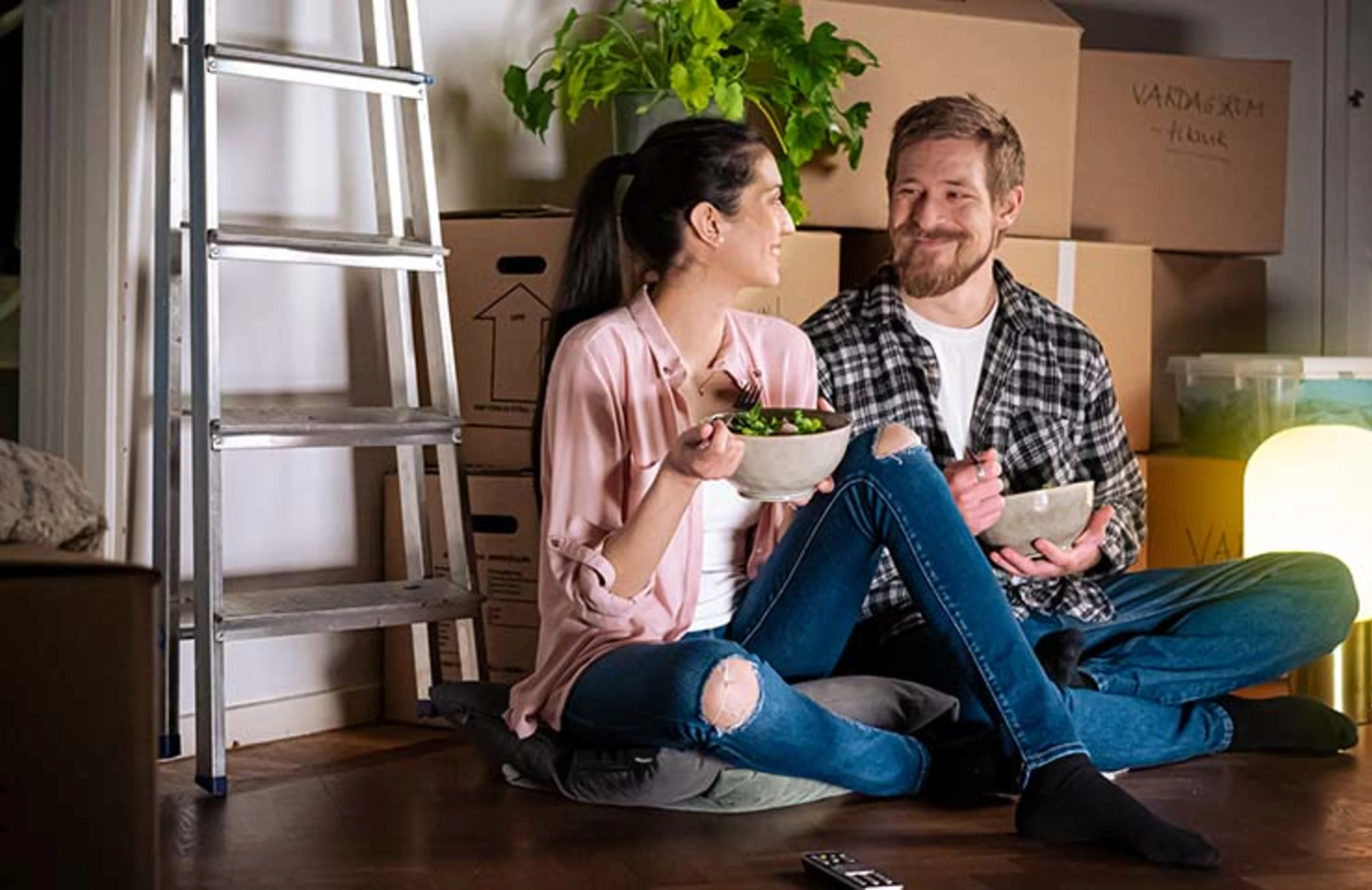 Ta med ditt elavtal när du flyttar – Byt adress med ditt elavtal | Bilden föreställer: Leende och nyinflyttat par äter på golvet bland flyttkartonger