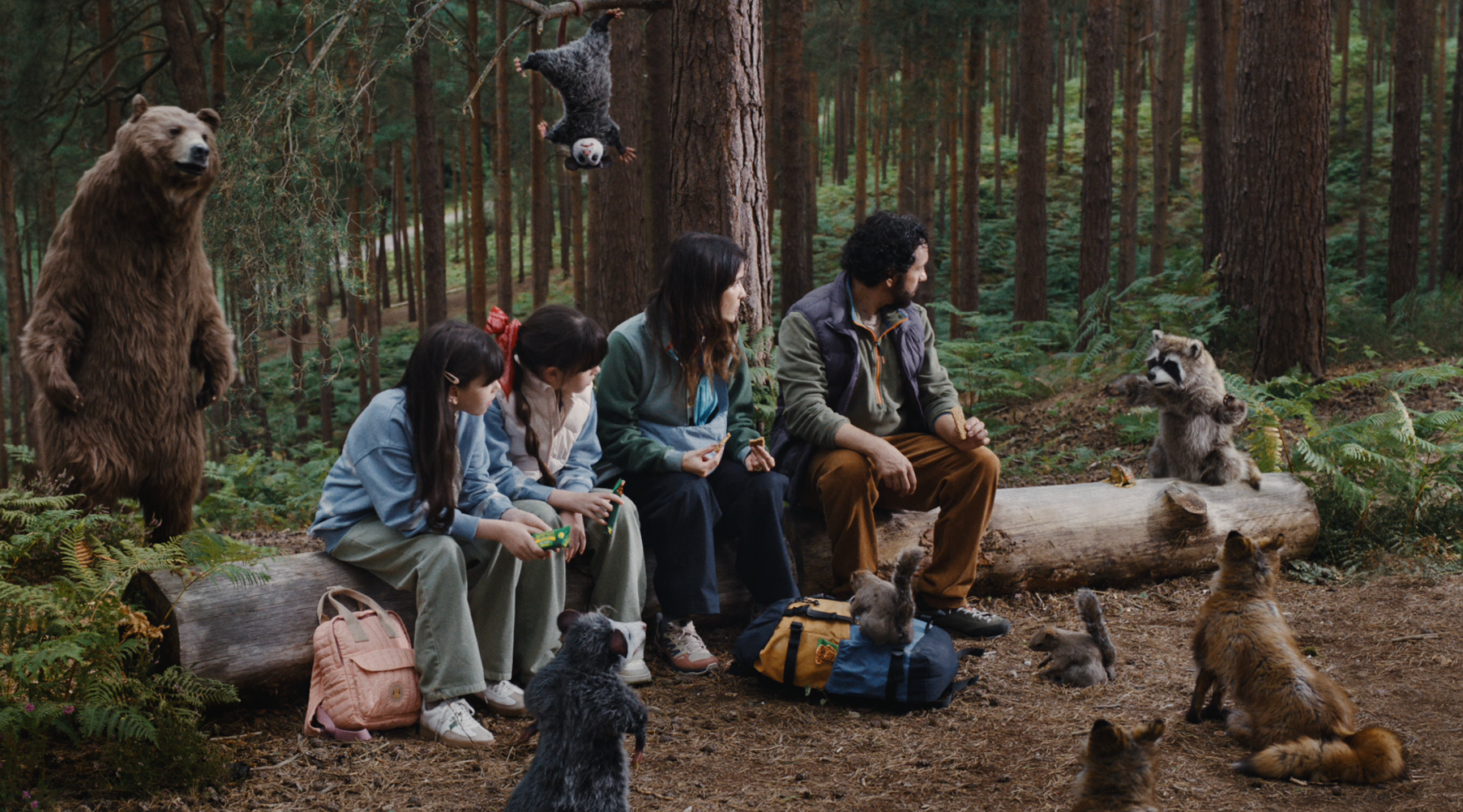 Nature Valley's we make nature delicious campaign puppets surrounding a family of four sitting on a log with their Nature Valley bars