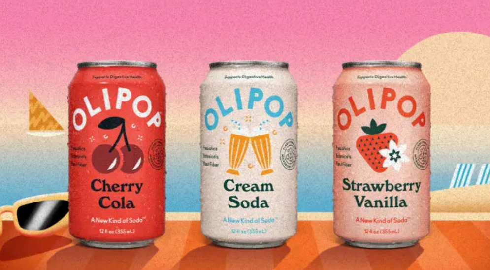 Three cans of soda including cherry, cream soda, and strawberry vanilla flavors sit on a table with a sunset in cartoon form behind them. 