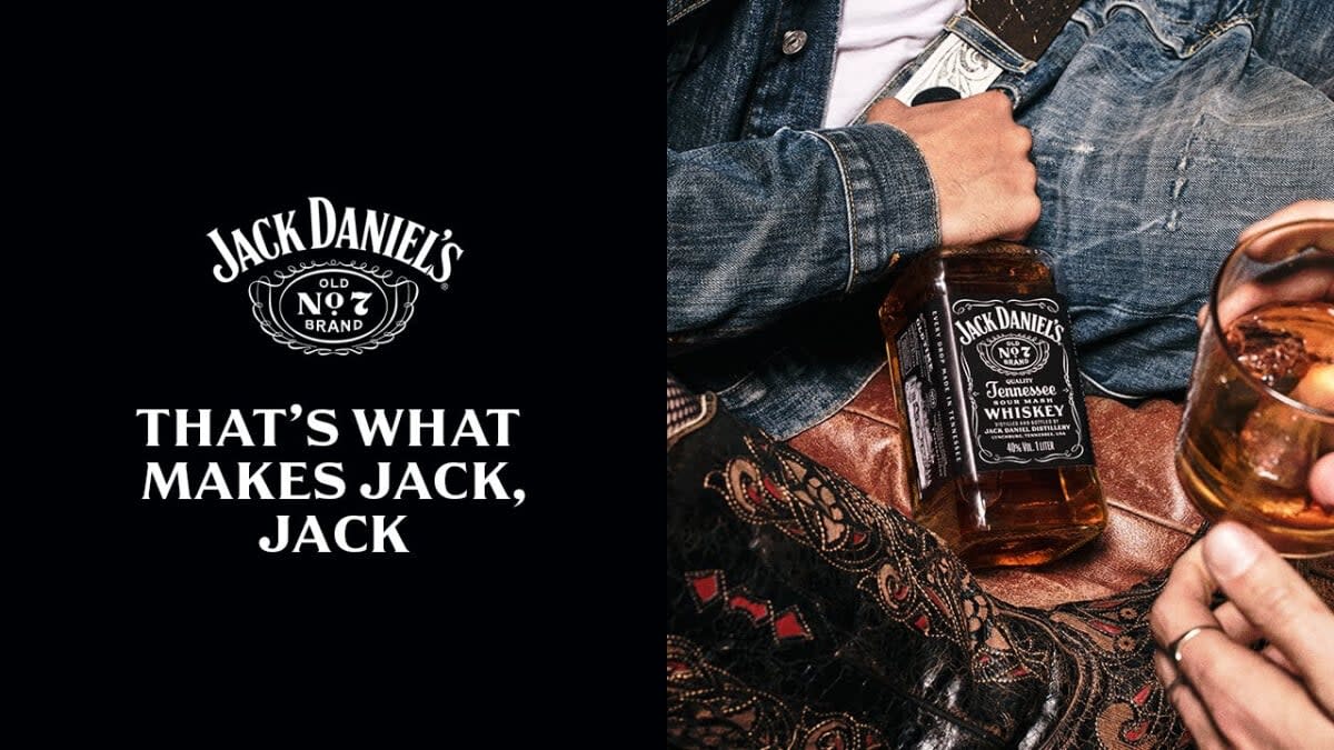 Split image with words “That’s what makes Jack, Jack” in white text over black background and image of a mans arm in jean outfit holding a bottle of Jack Daniel’s with a full glass nearby  