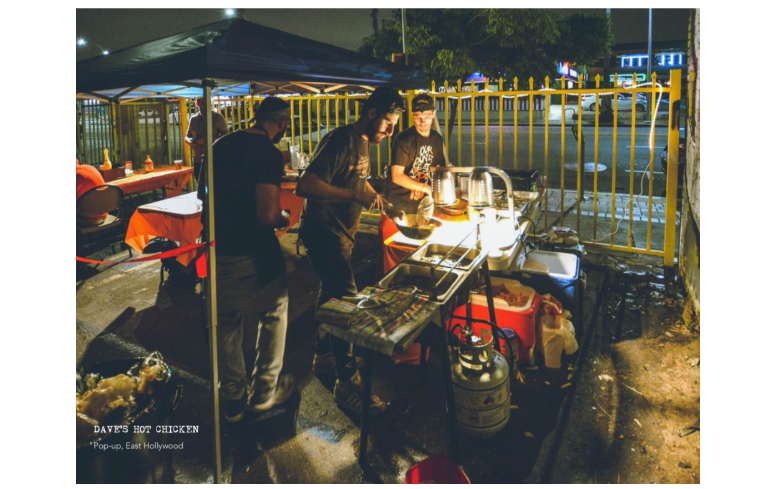 Photo of three men standing at an outdoor set up for cooking and selling chicken in the dark