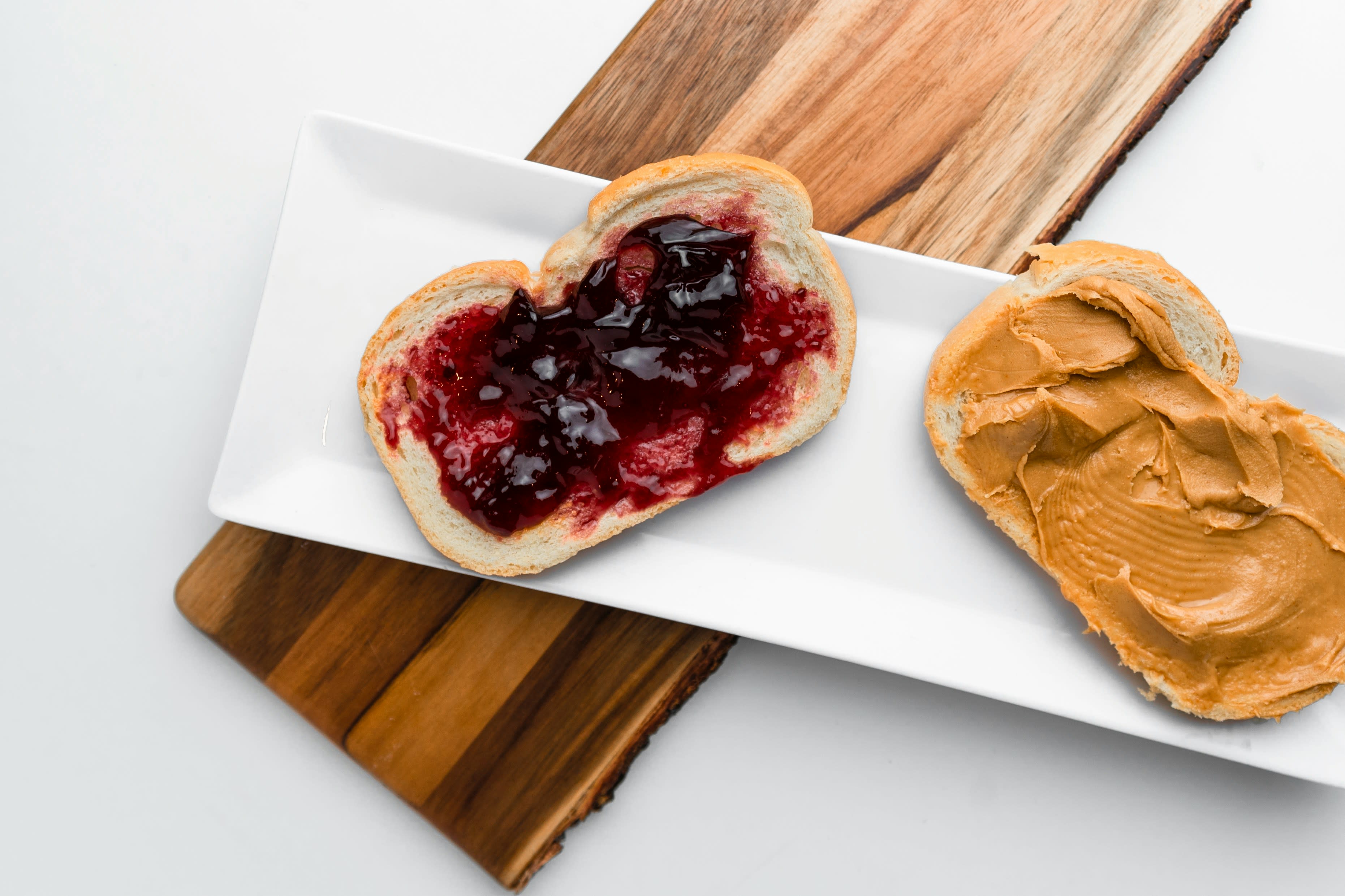 Image of two slices of bread with one covered in jelly and one covered in peanut butter next to each other on a plate