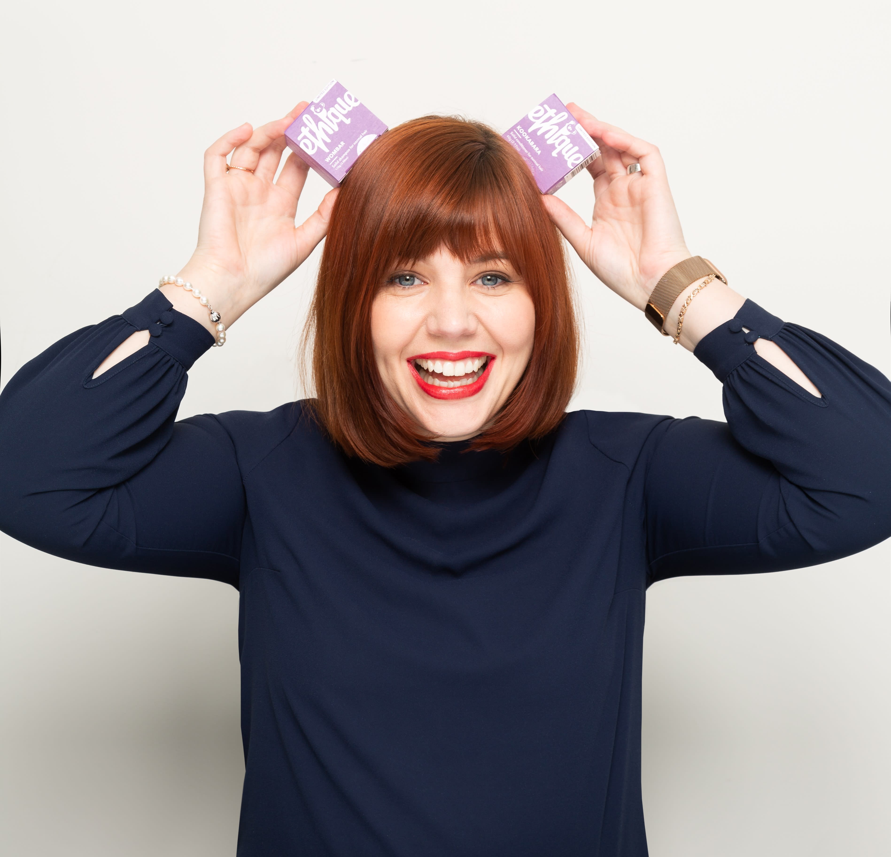 Ethique founder poses in front of white background holding up two boxes of solid beauty bars